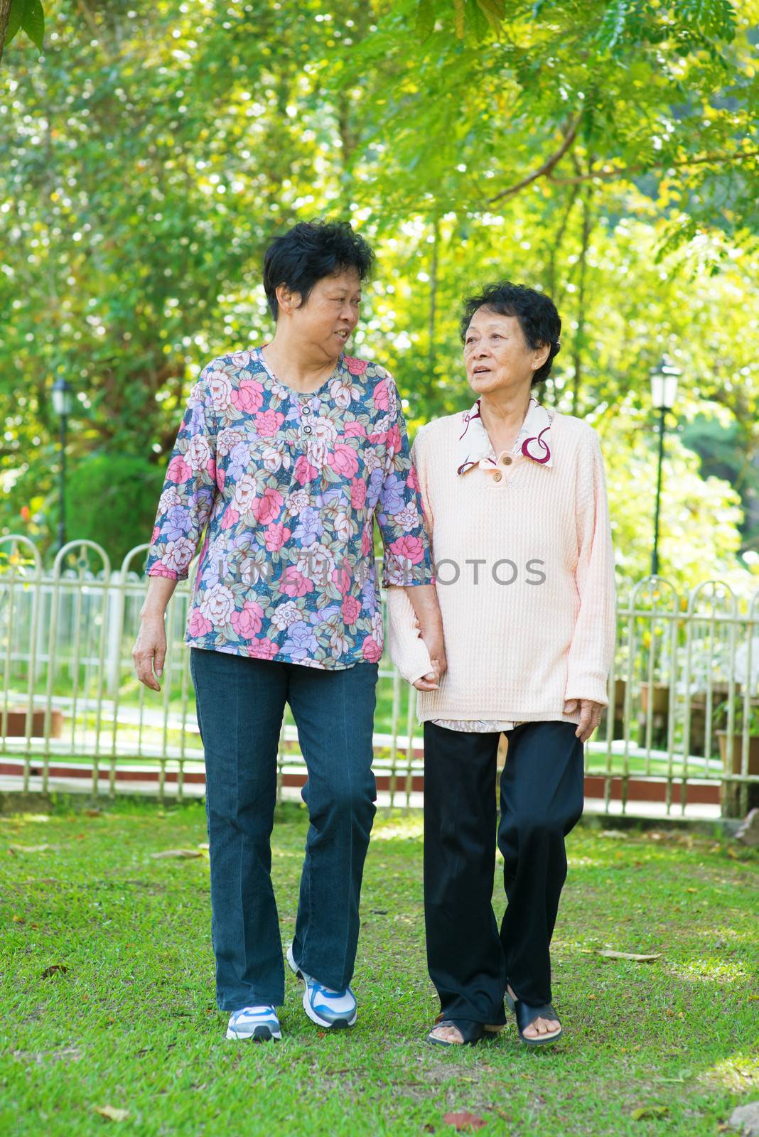Asian 80s old mother and 60s senior daughter holding hands walking at outdoor park.