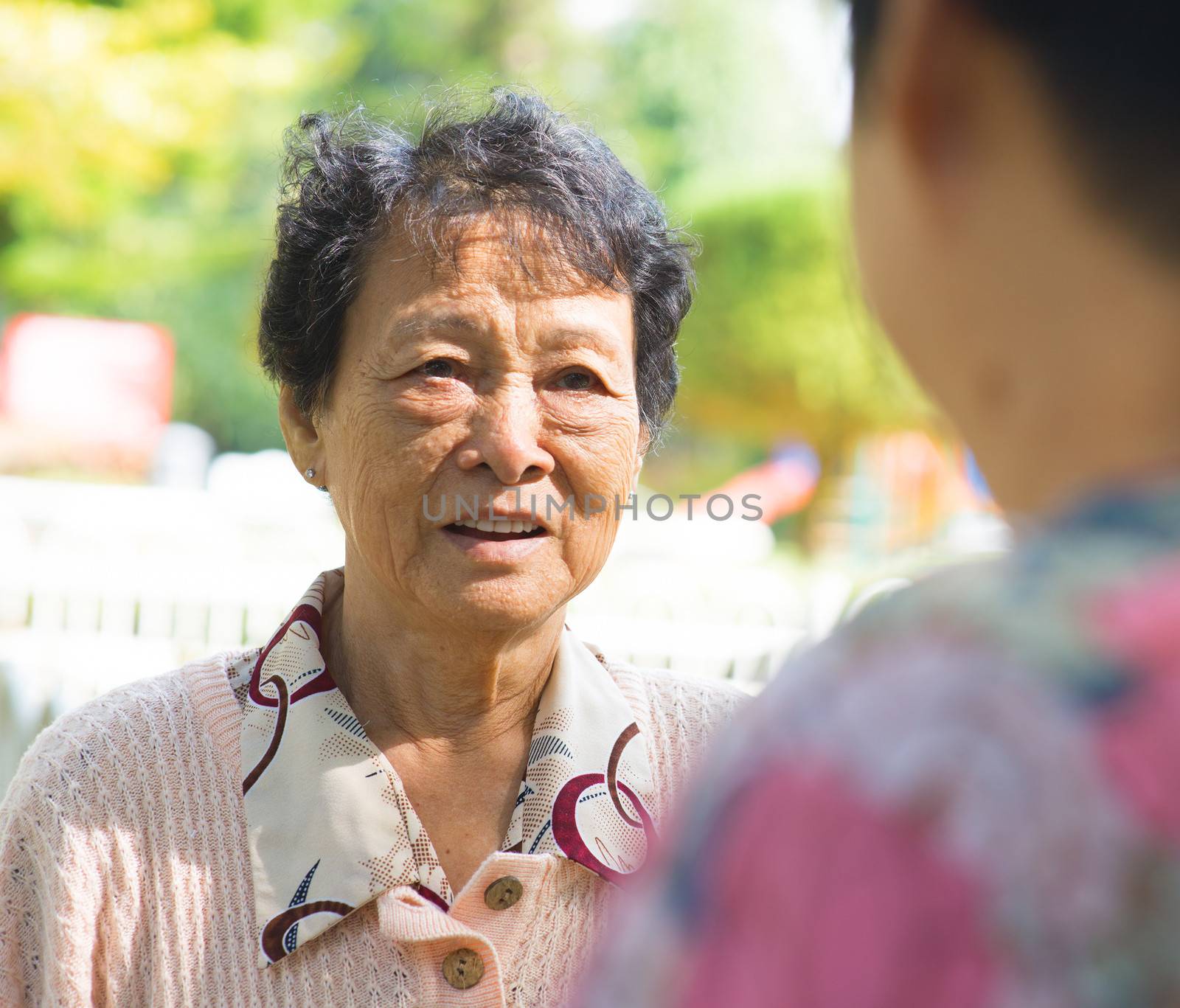 Asian 80s senior women having conversation at outdoor park, candid shot.
