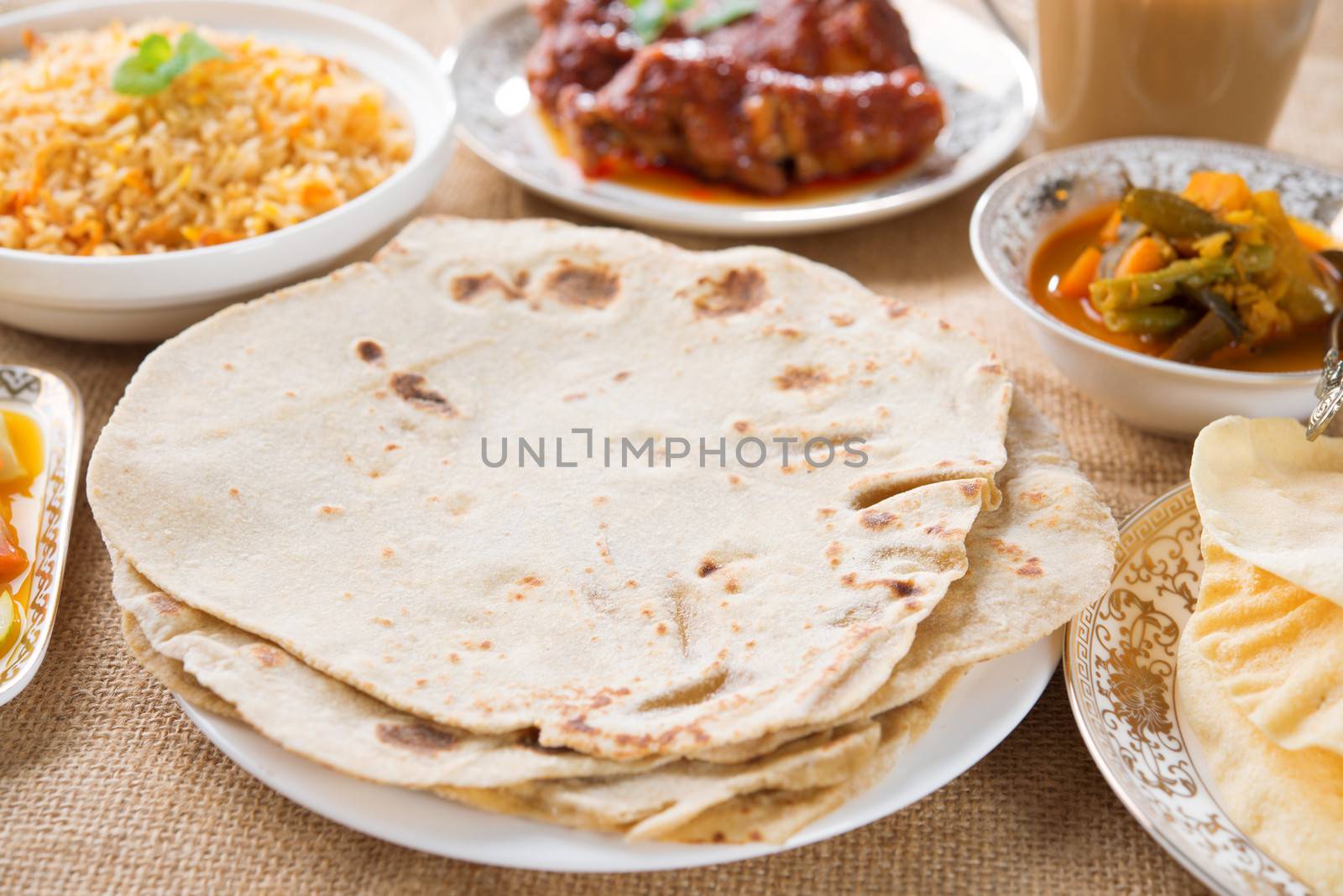 Chapatti roti, curry chicken, biryani rice, salad, masala milk tea and papadom. Indian food on dining table.