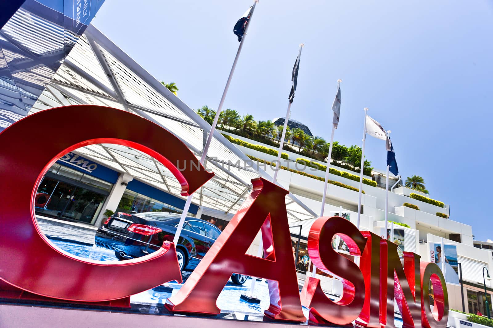 Close up view of a large red Casino sign photographed at a very oblique angle with a modern building and flags in the background