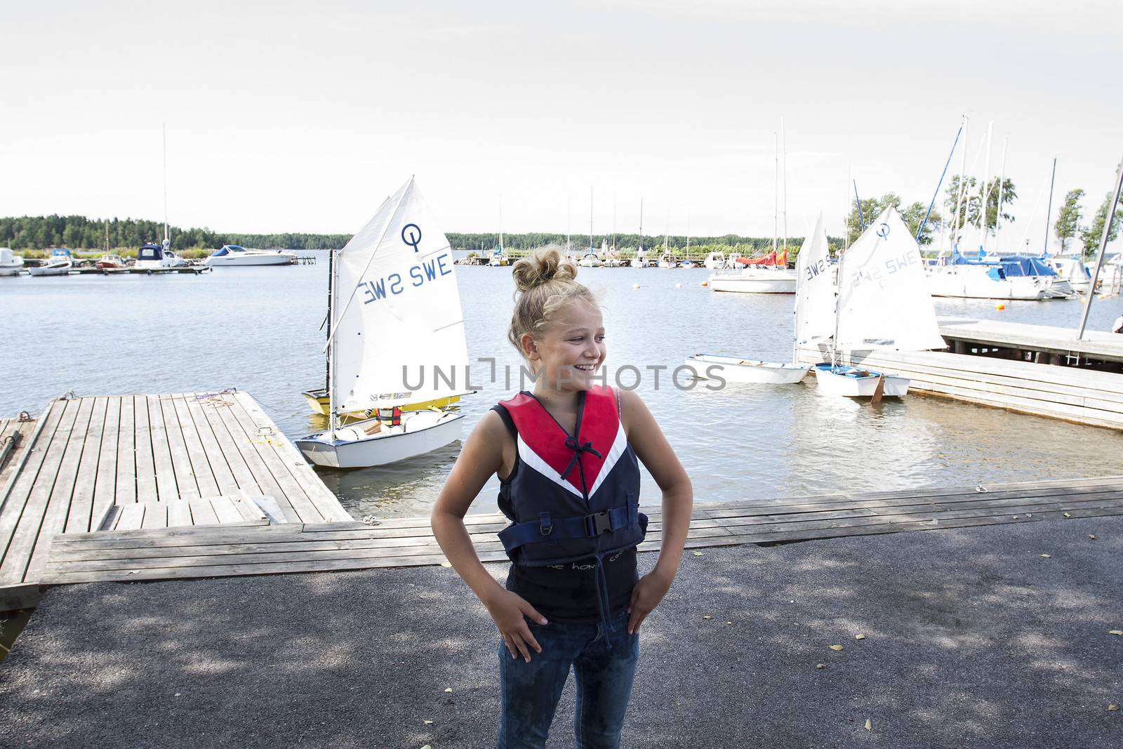 Child standing on a pier in front of optimist sailing boats