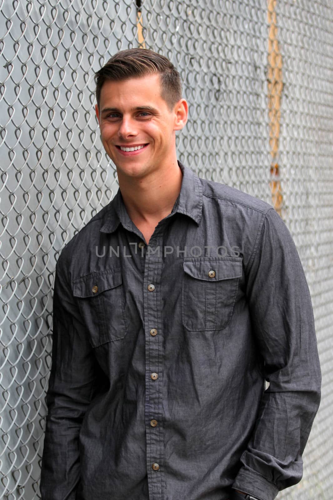 Portrait of a man standing in front of a chain link fence.