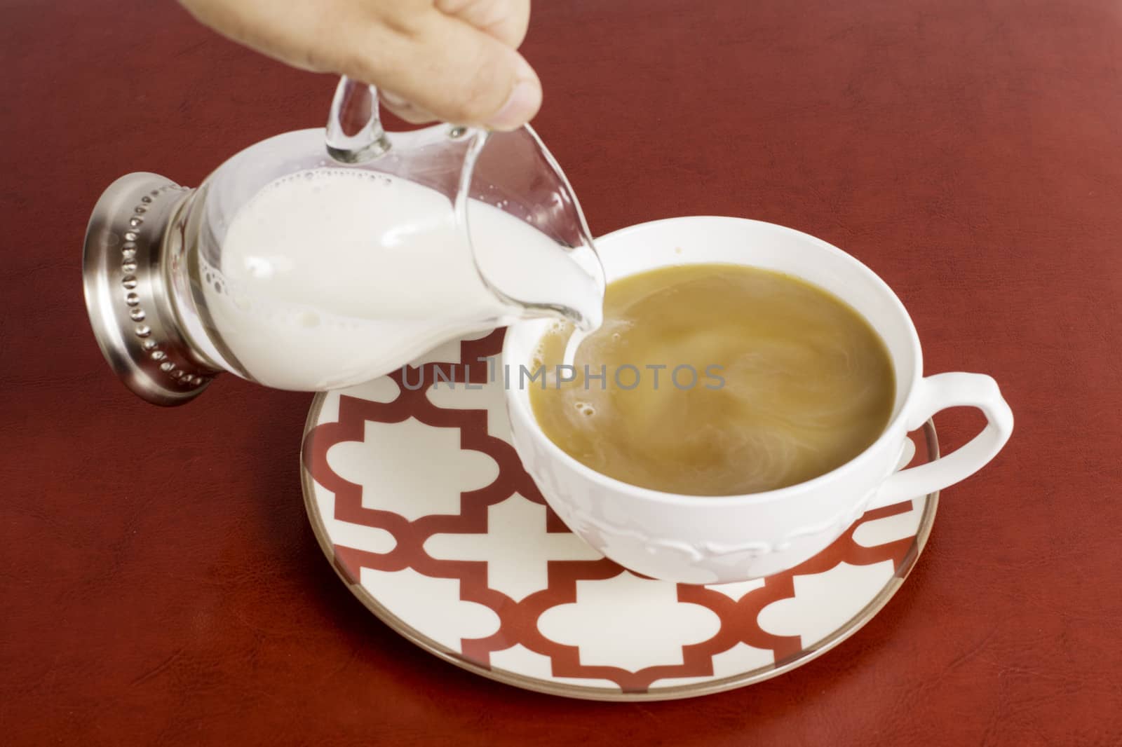 A hand pouring cream into a cup of coffee.