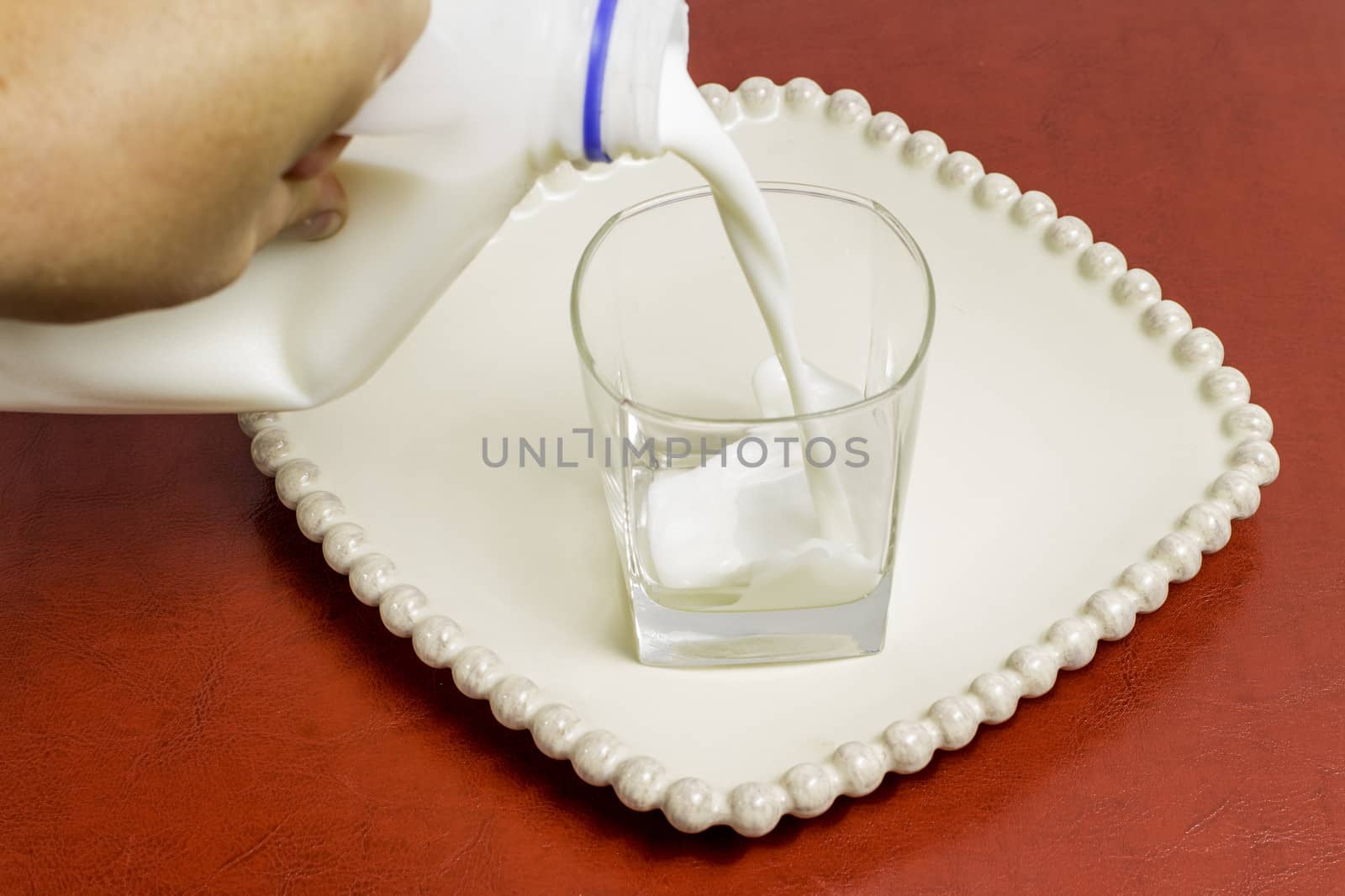 A glass sitting on a plate with milk from a jug being poured.