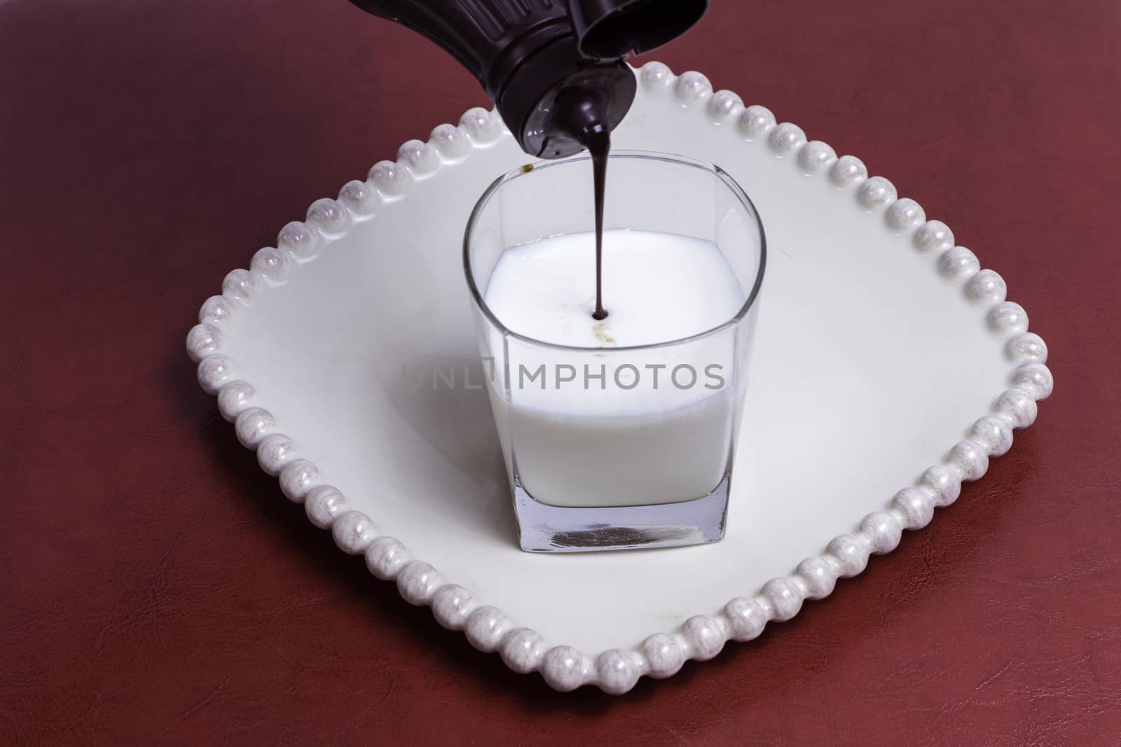 Chocolate syrup being added to a fresh glass of milk.