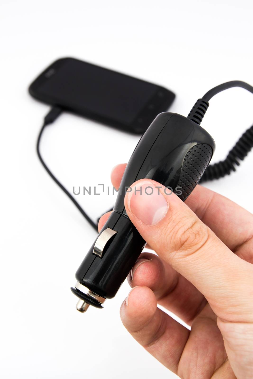 Hand holding car charger. Cell phone in background