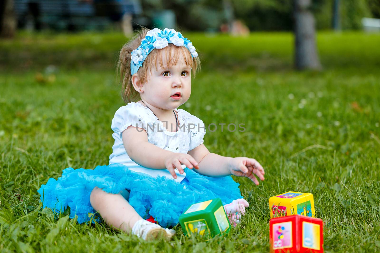 Little girl sitting on the grass and playing with dice in the park