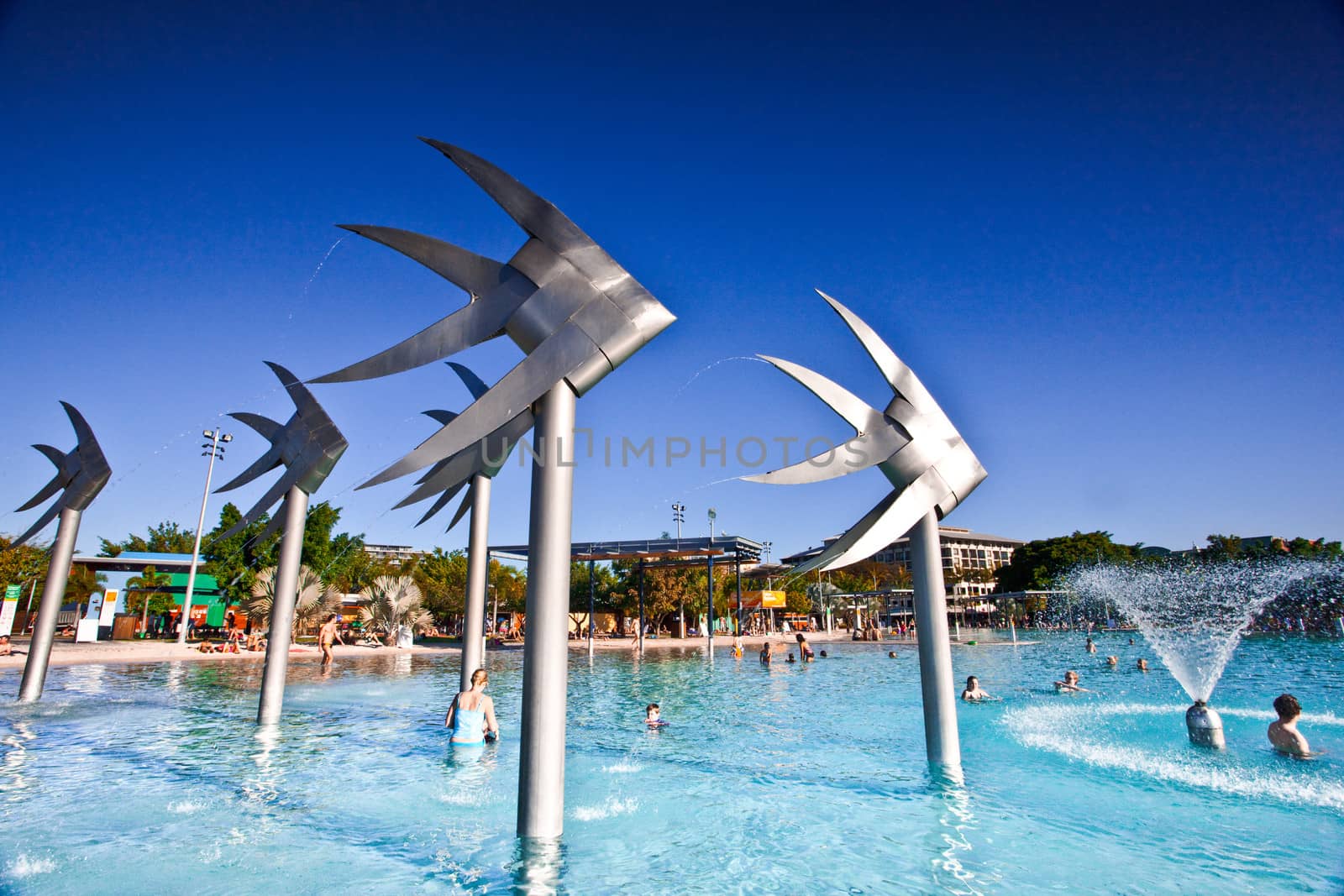Swimming lagoon and steel Fish Sculpture in Cairns, Australia with people enjoying the summer sun frolicking in the water