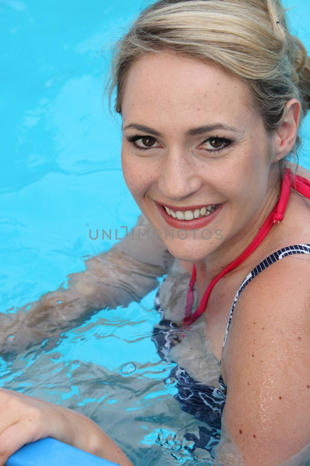 Beautiful young blond woman swiming in a cool blue inviting swimming pool on a hot summer day