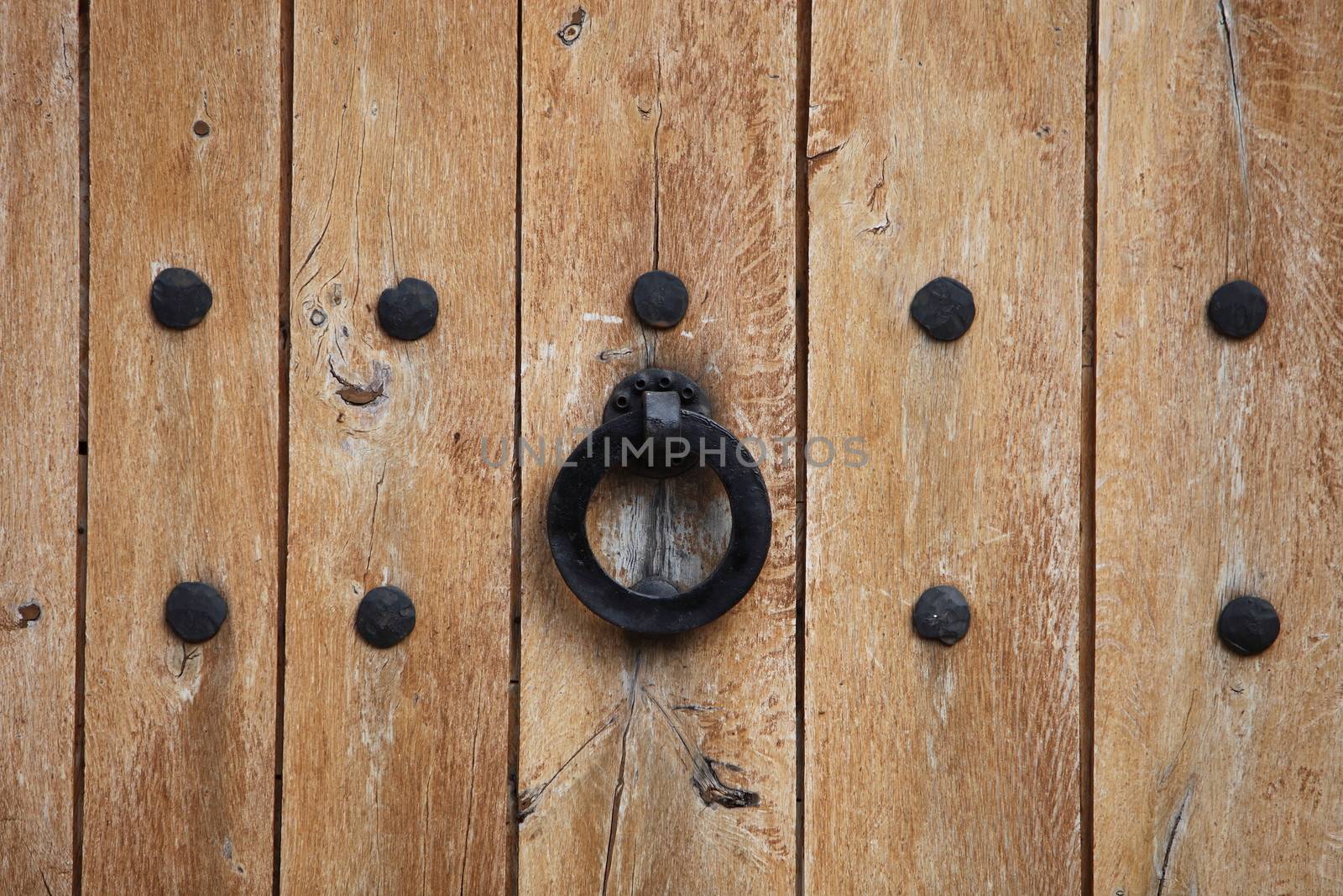 Door handle or knocker in the form of an iron ring on an old wooden door between two rows of studs