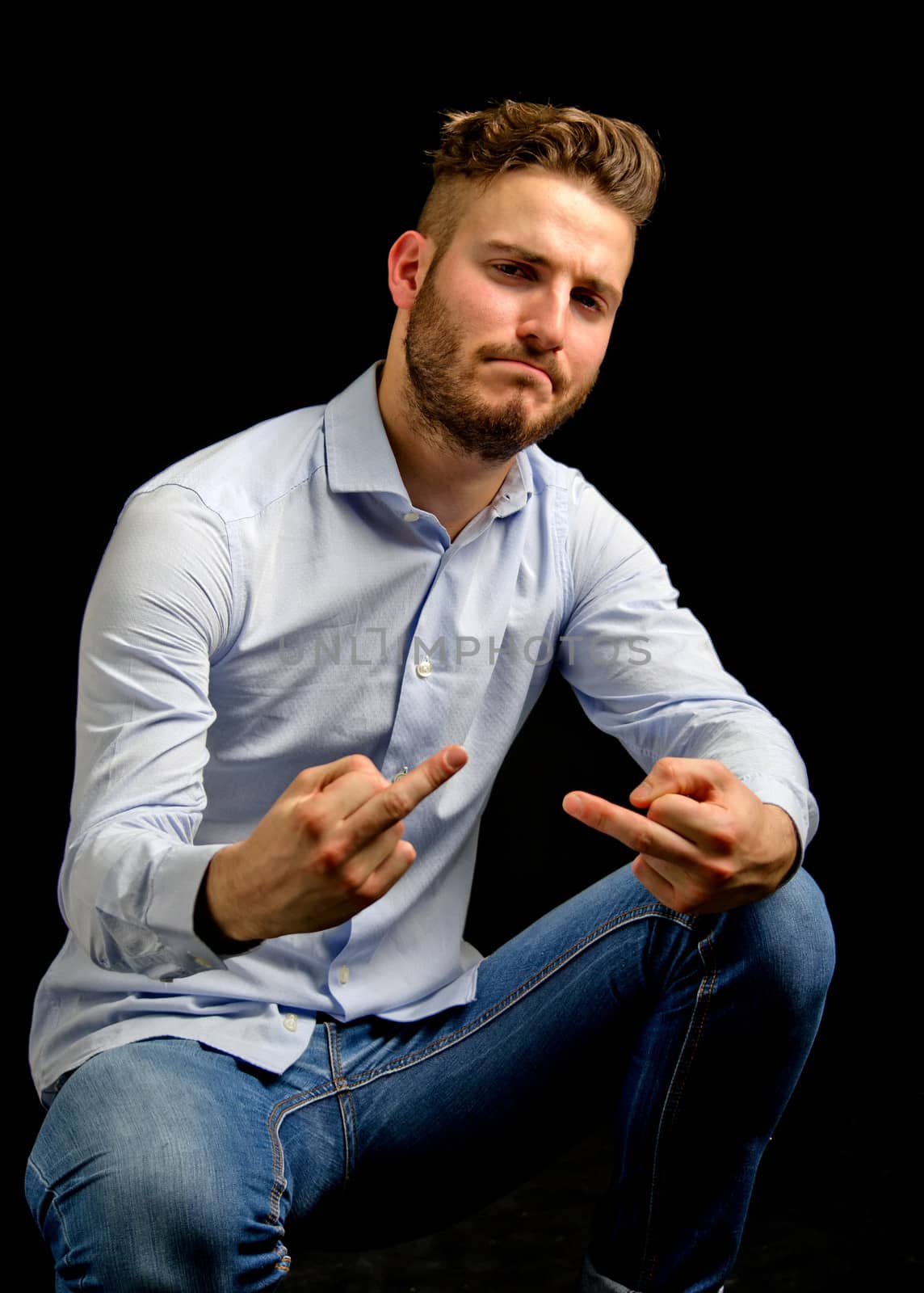 Friendly young man doing 'fuck you' gesture with middle fingers, isolated on black background
