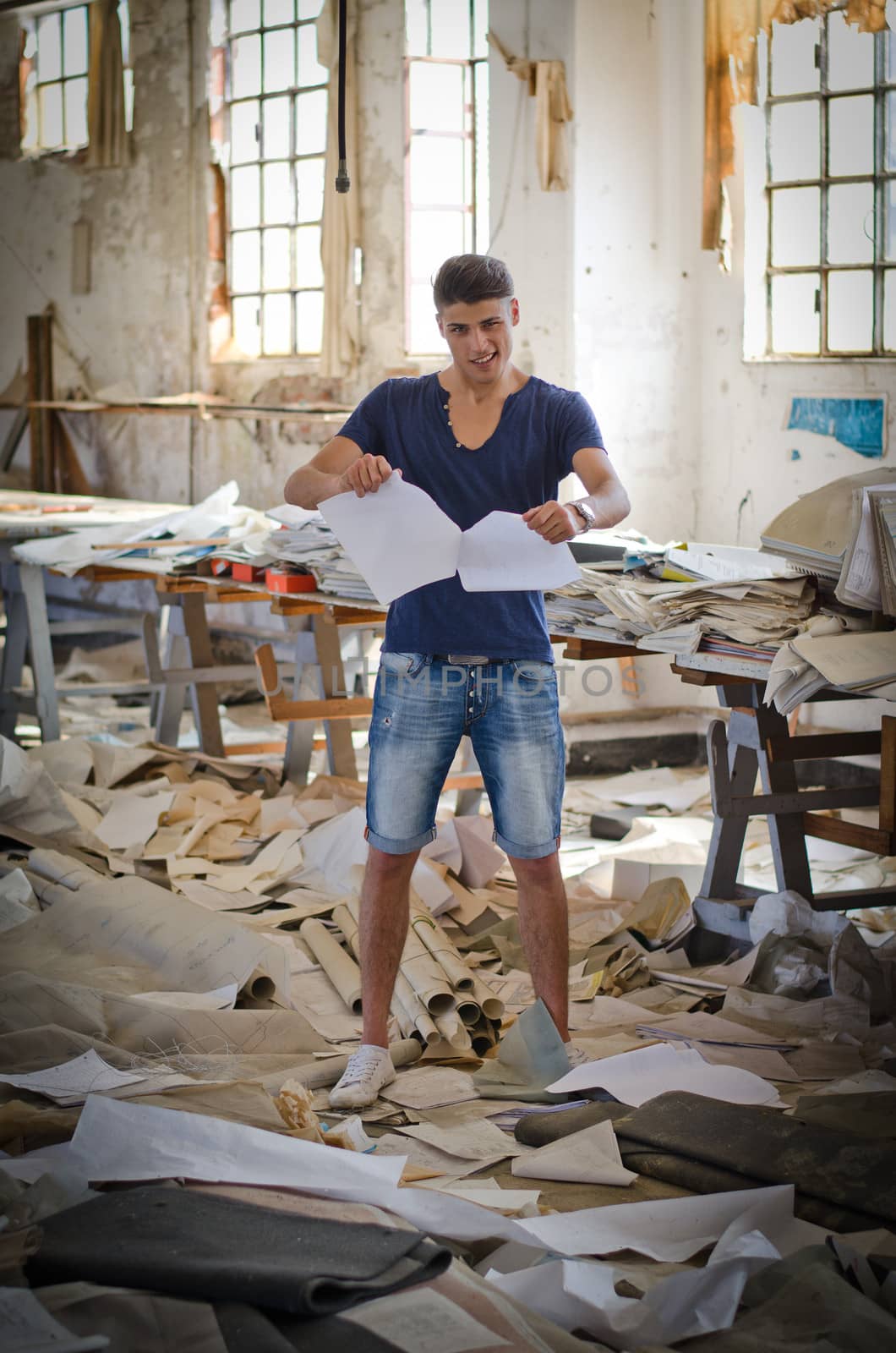 Attractive young man in messy office or working place tearing up paper sheets