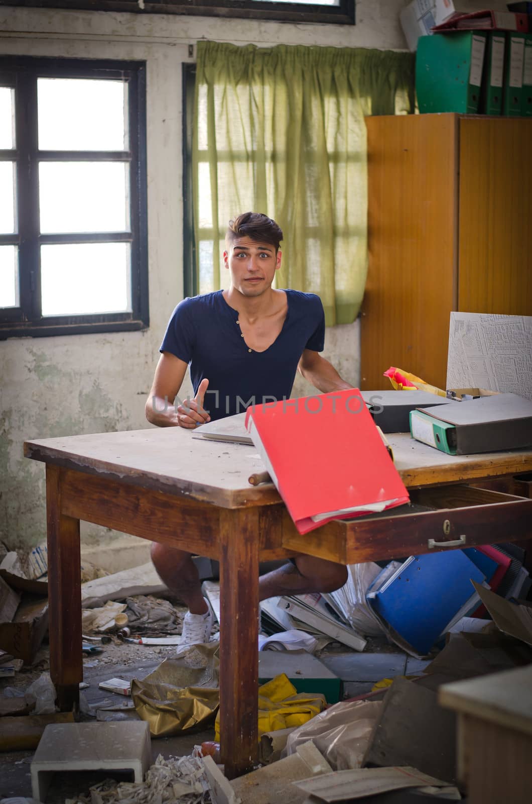 Young man in very messy office looking lost or confused