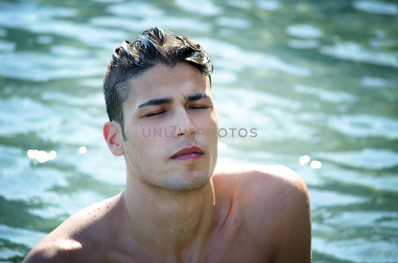 Handsome young man coming out of water with wet hair, eyes closed