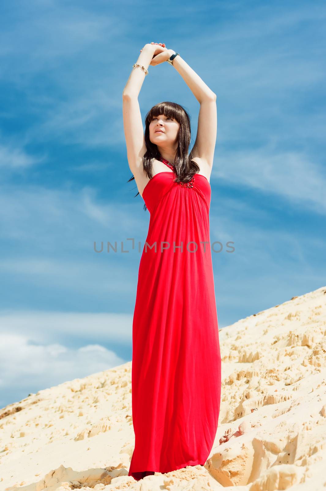 A girl in a red dress posing on a sand dune