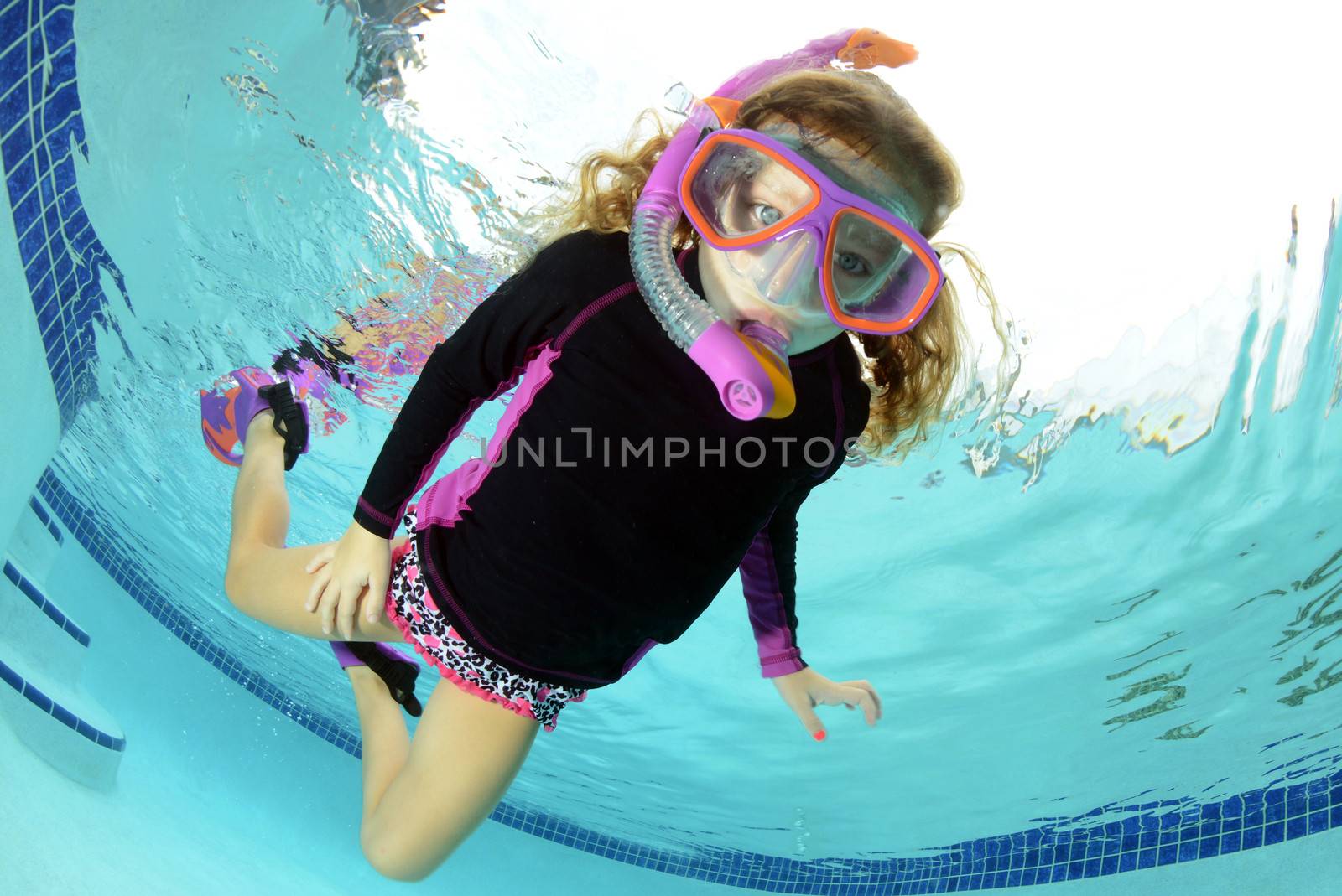 young girl swimming in pool with snorkel and goggles