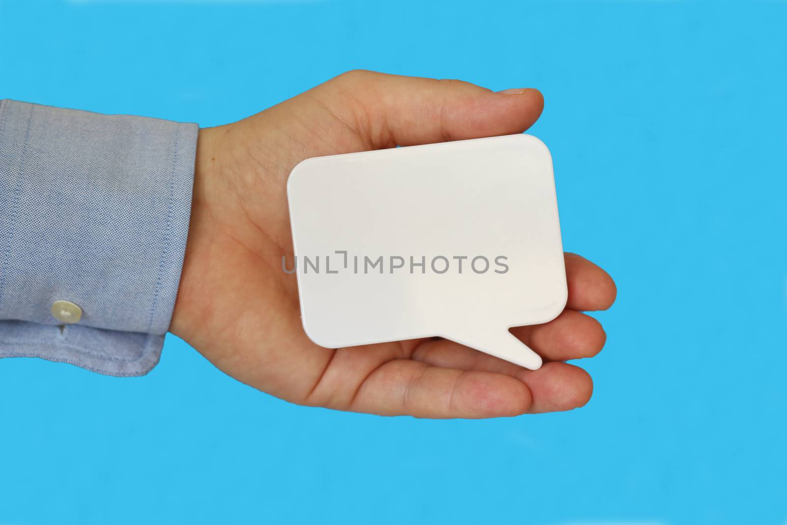 Man holding up a small blank white rectangular speech bubble with copyspace for your text in his hand over a blue background Man holding up a small blank white rectangular speech bubble with copyspace for your text in his hand over a blue background