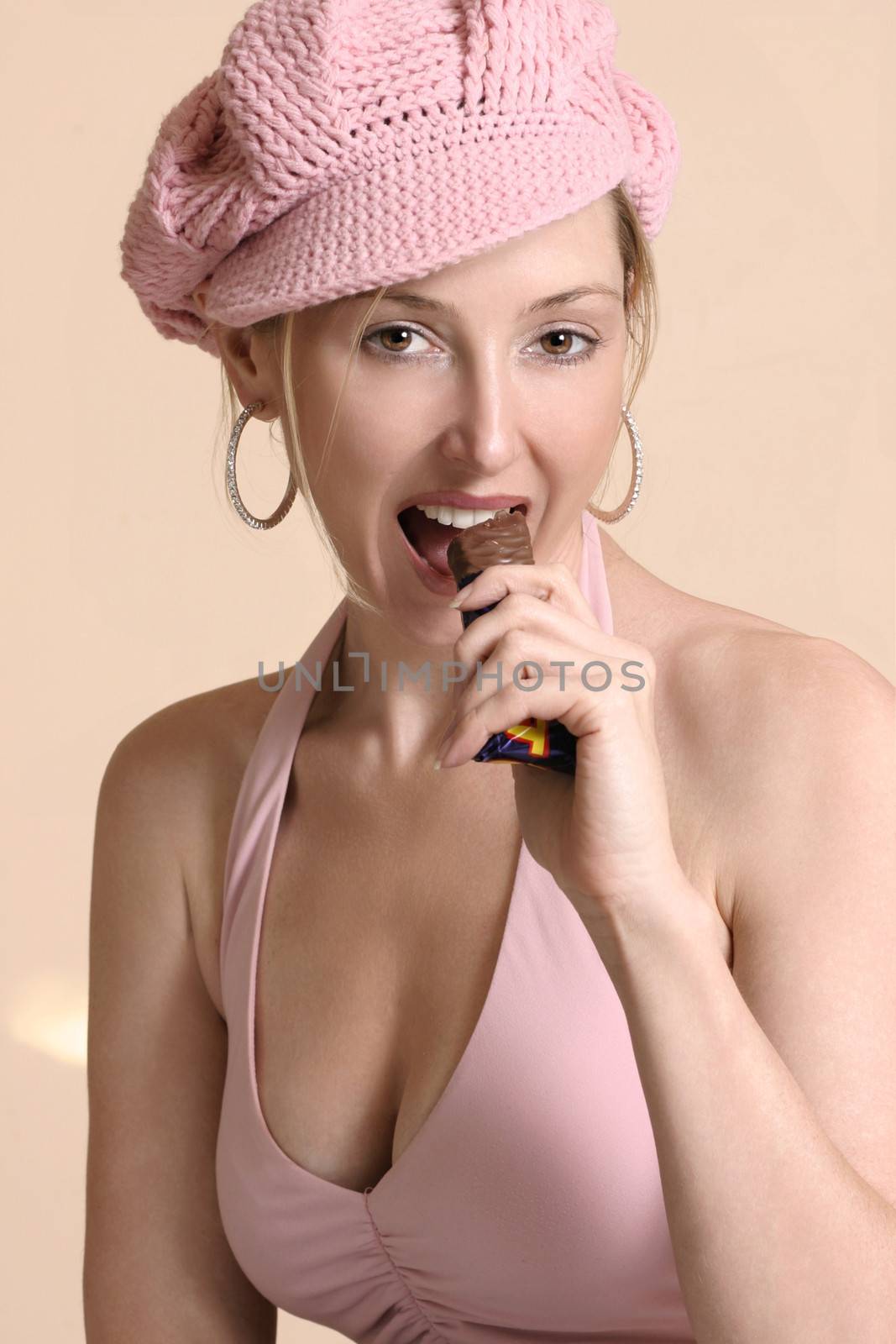 A woman eating a delicious chocolate bar.  She is wearing a pink hat and halter