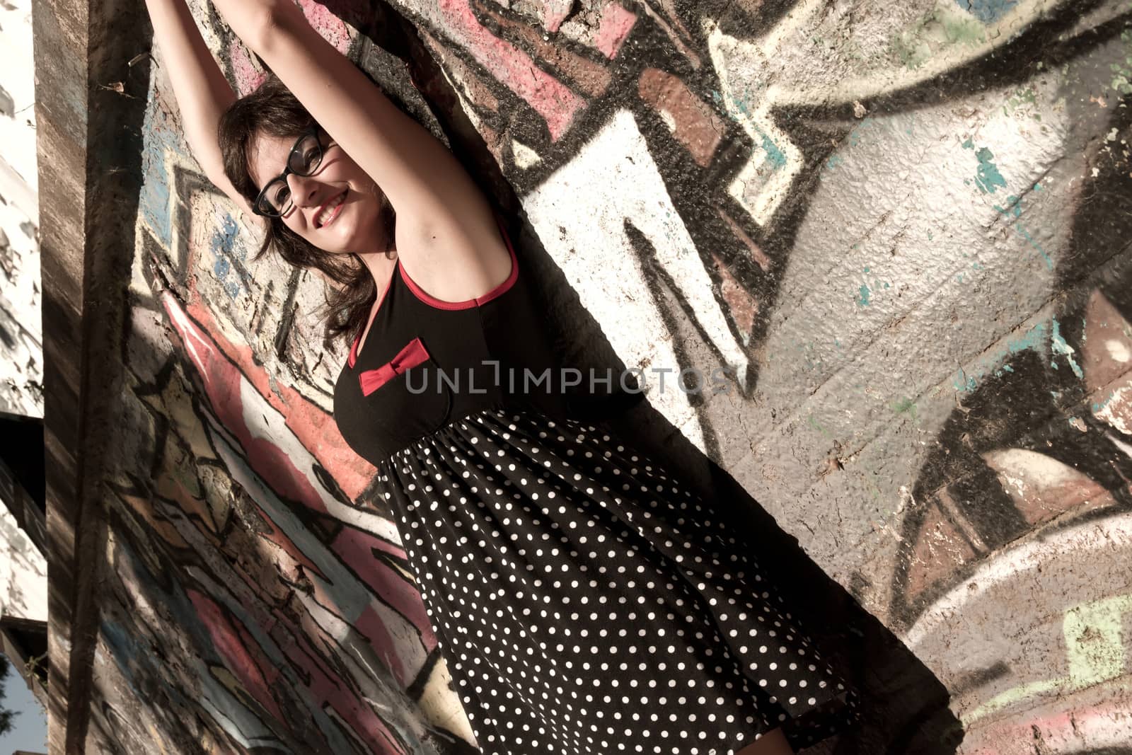 A vintage style dressed girl leaning at a graffiti wall and enjoying the sunlight.