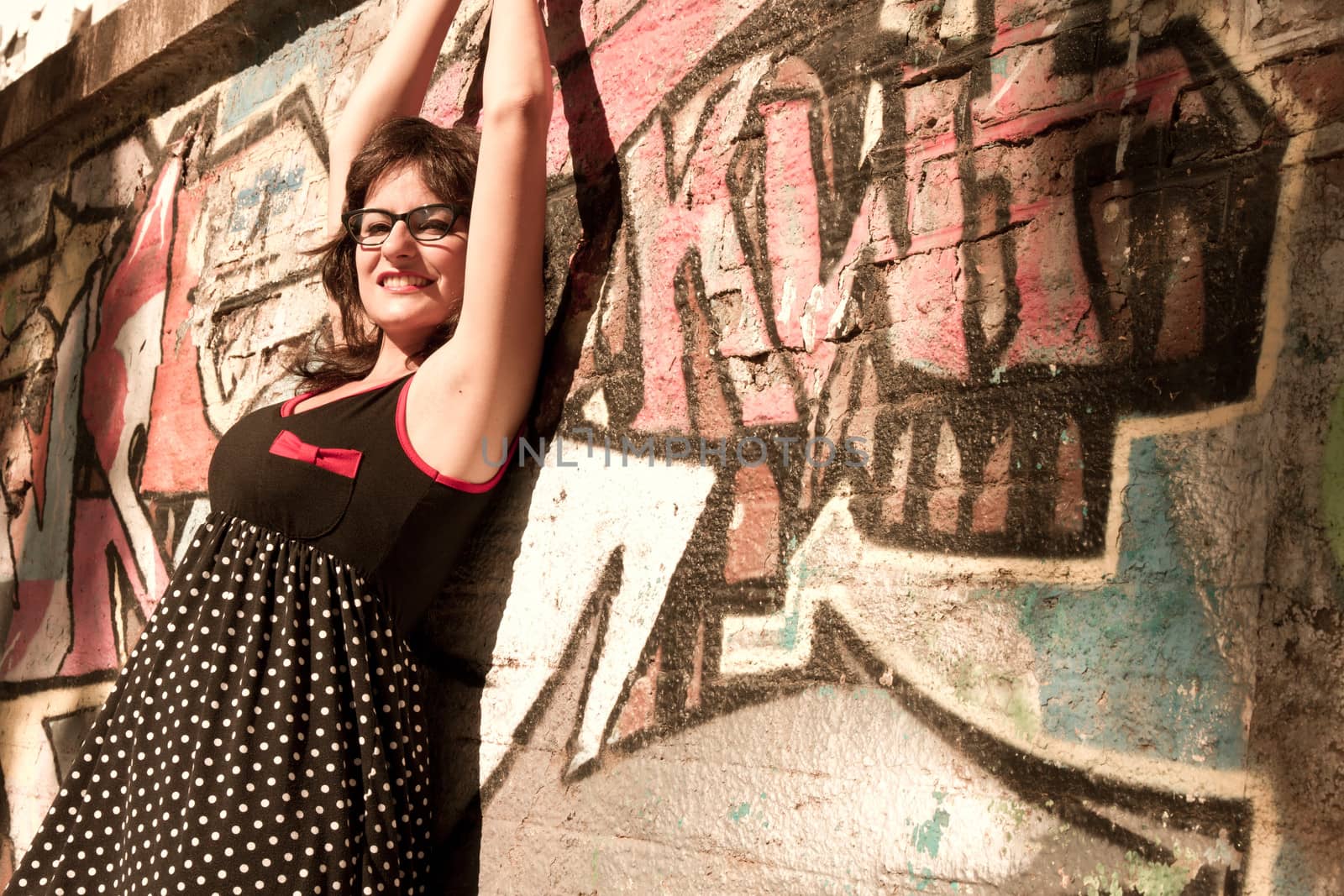 A vintage style dressed girl leaning at a graffiti wall and enjoying the sunlight.