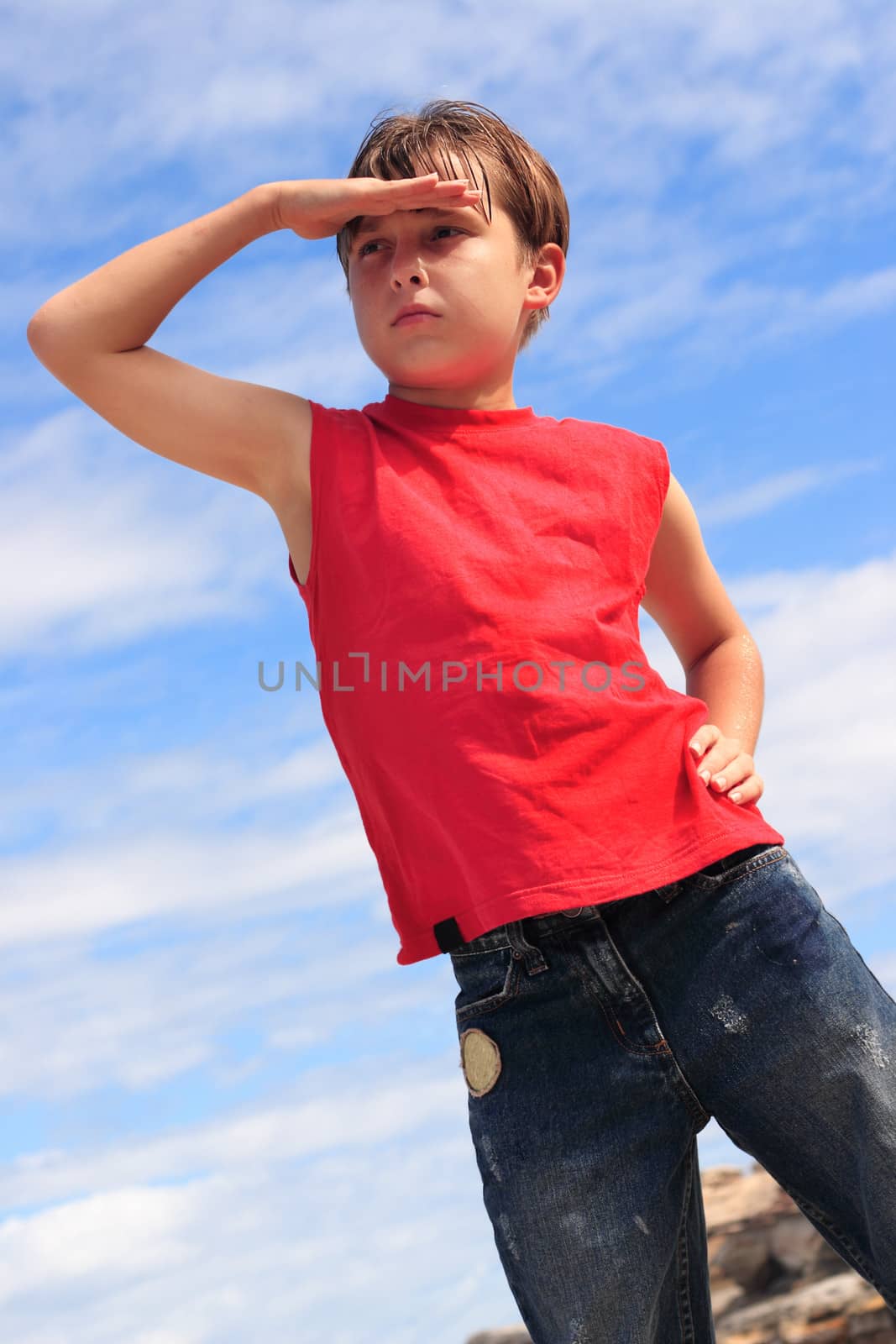 A boy in the summer sunshine with hand to forehead, searching and looking out to the distance