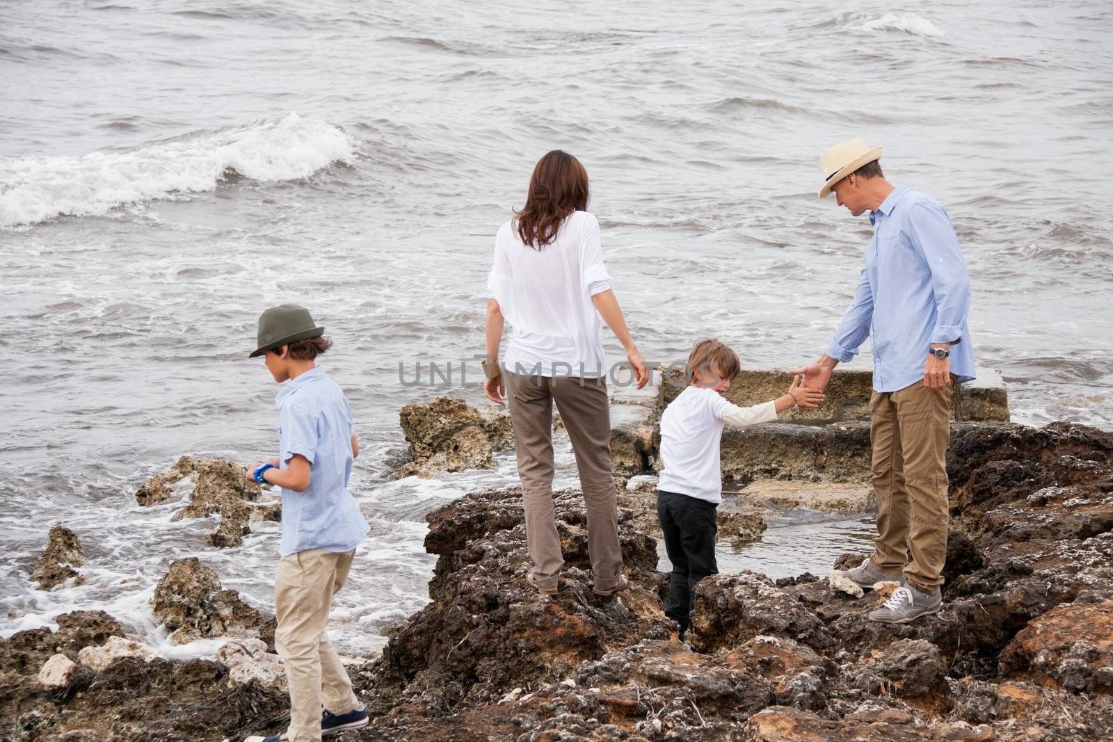 happy family sitting on rock and watching the ocean waves by juniart