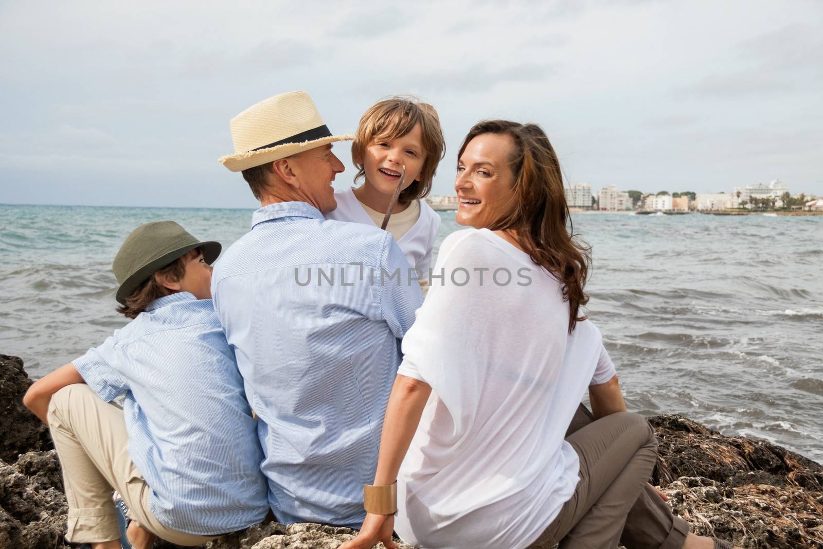 happy family sitting on rock and watching the ocean waves by juniart