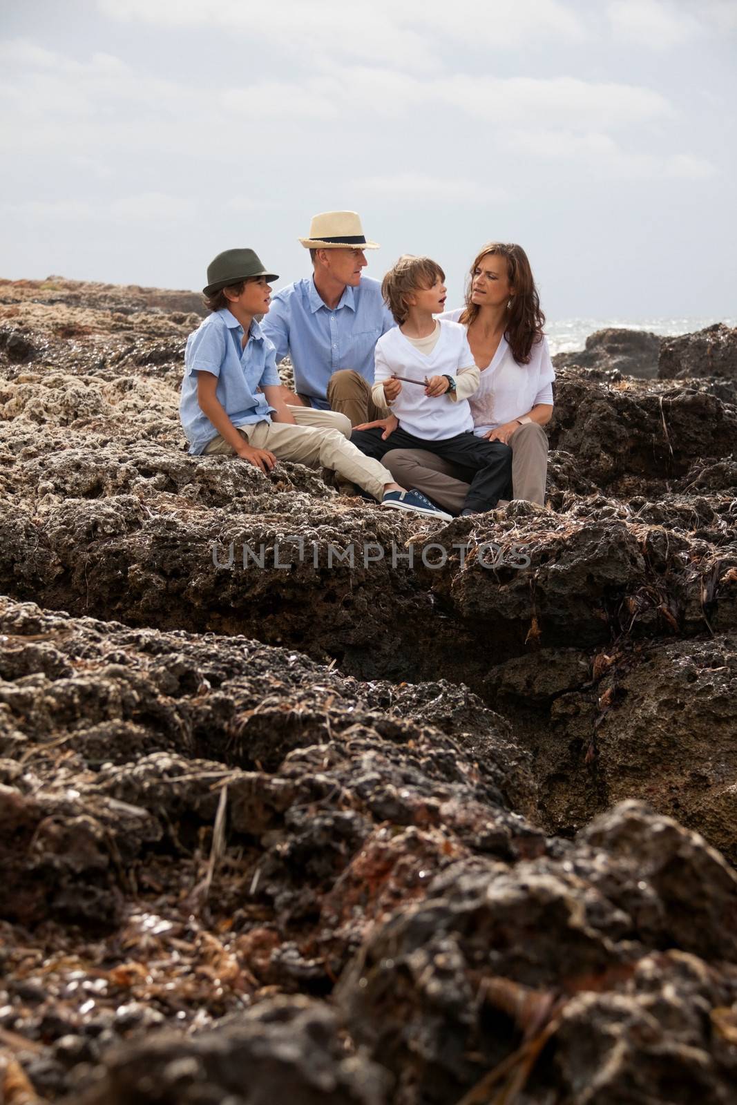 happy family sitting on rock and watching the ocean waves by juniart