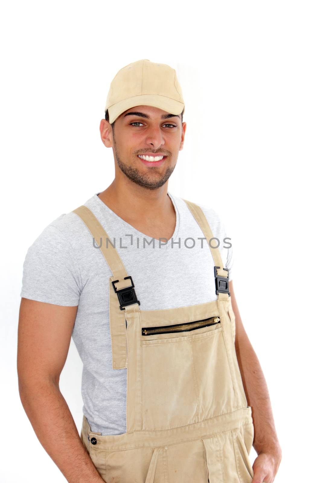 Handsome man in cap and dungarees standing smiling confidently at the camera, isolated on white