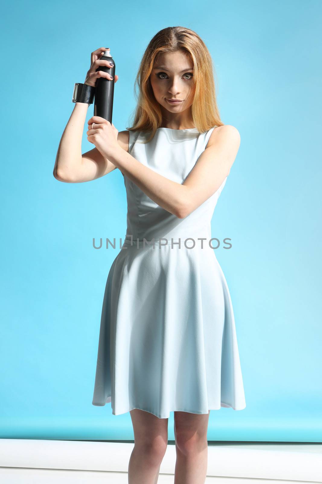 Beautiful girl in a white dress holding a bottle with hairspray
