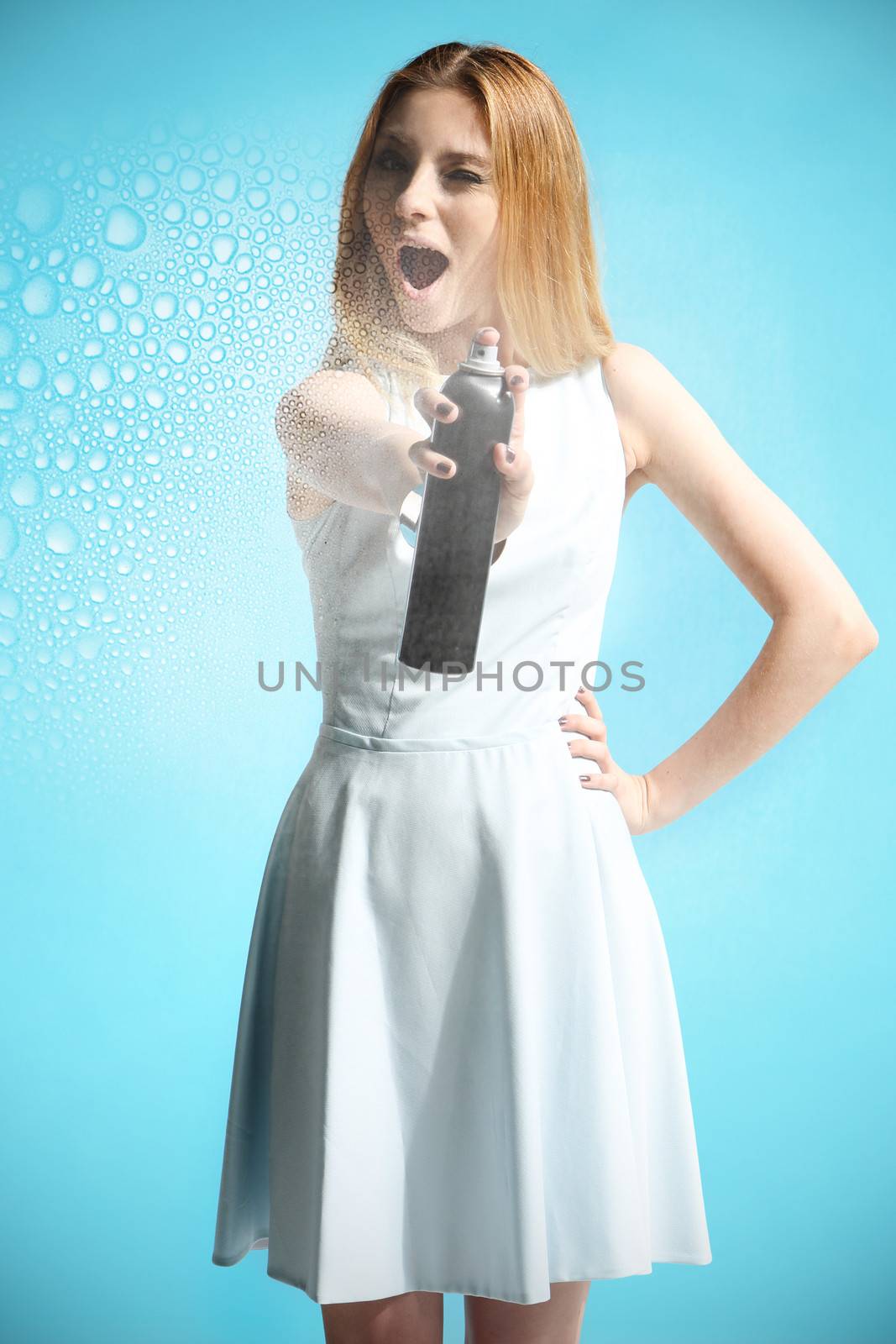 Beautiful girl in a white dress holding a bottle with hairspray by robert_przybysz