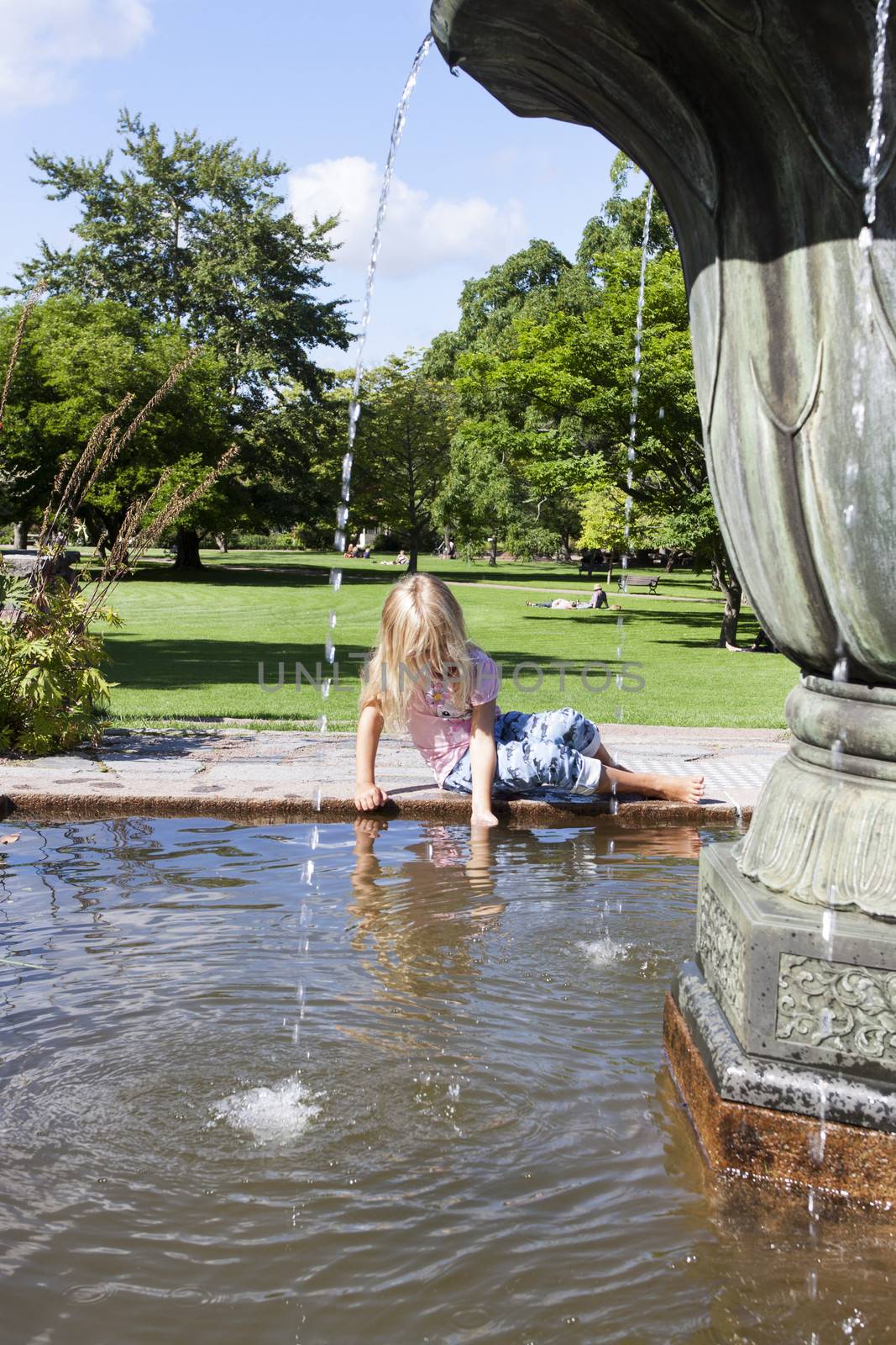 A child sitting on the edge of the fountain playing with the water