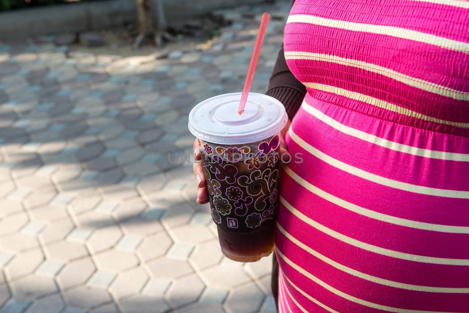 Asian pregnant woman holding a cup of softdrink, taken on a sunny day