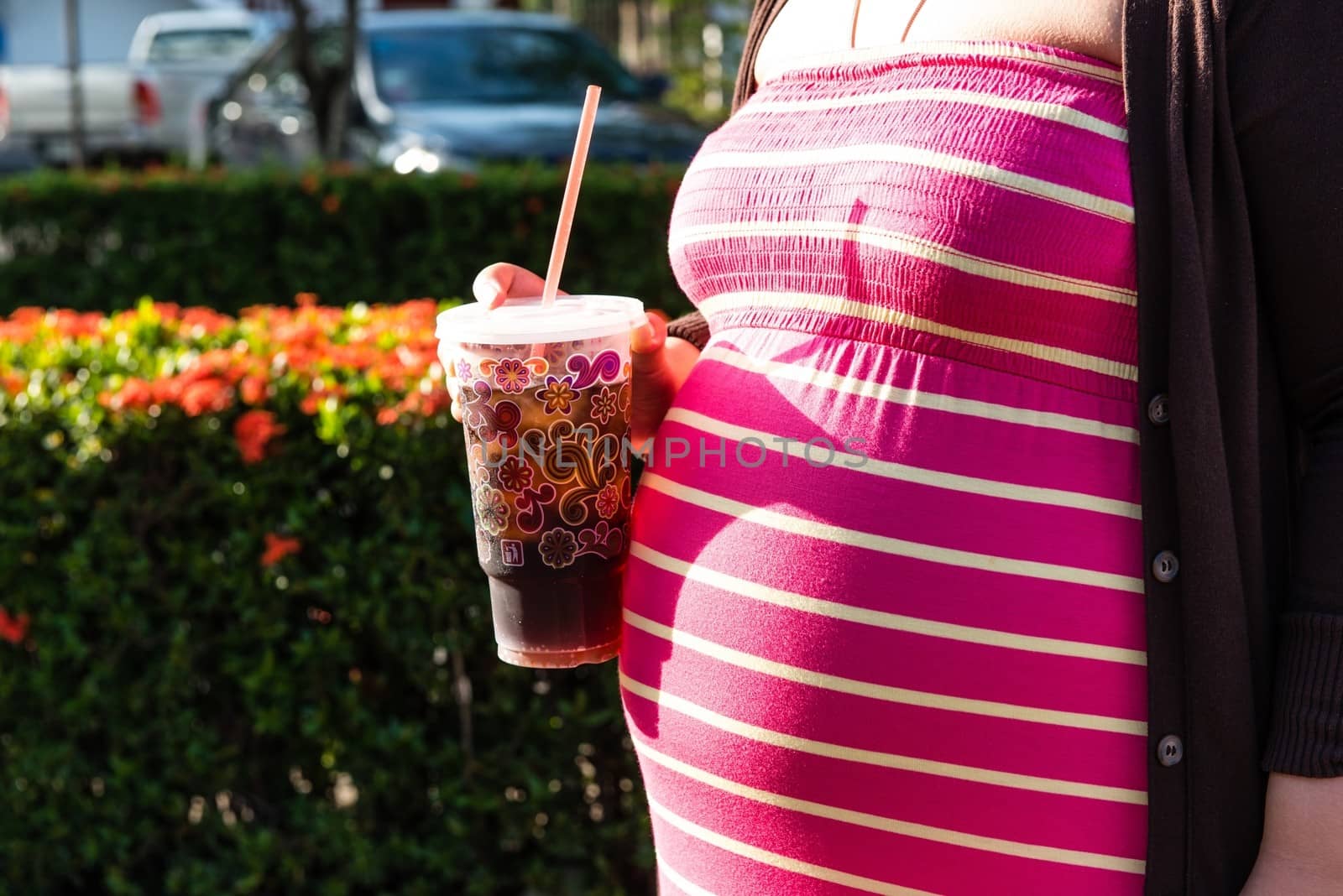 Asian pregnant woman holding a cup of softdrink, taken on a sunny day