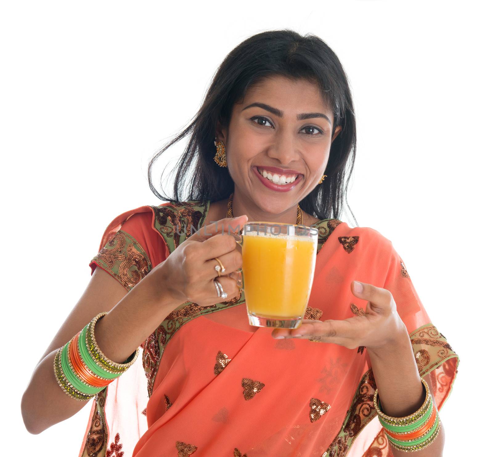 Happy traditional Indian woman in sari drinking a glass of orange juice, isolated on white background.