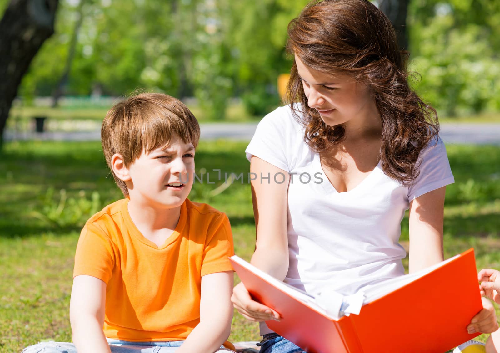 boy and a woman in a summer park reading a book together