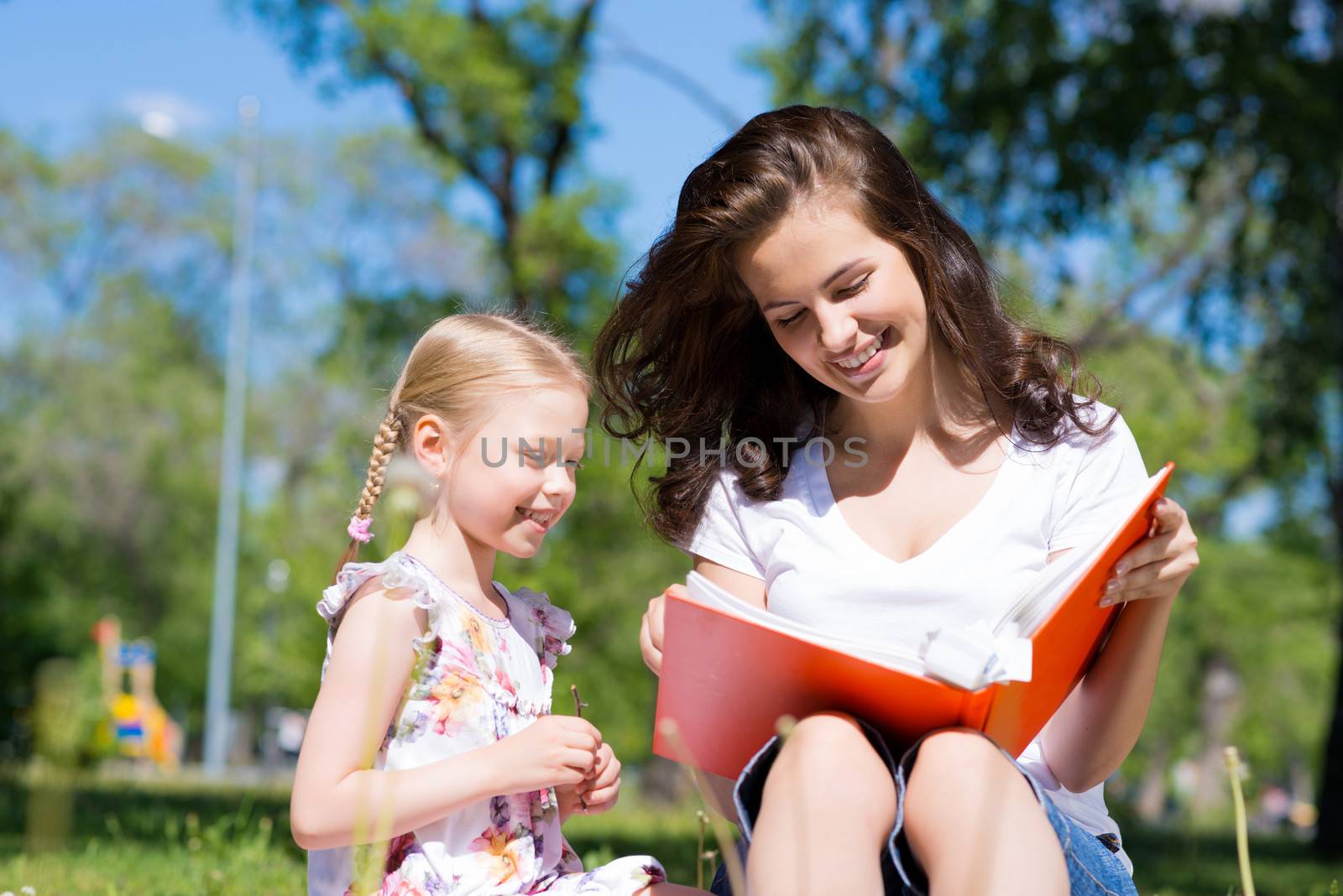 girl with the teacher reading a book together in the summer park