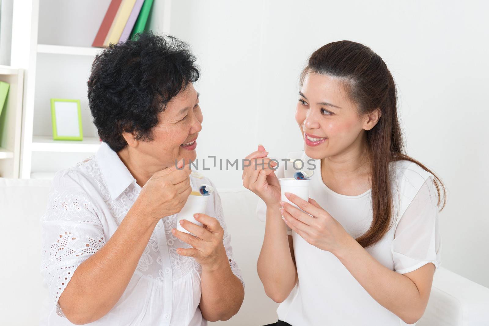 Eating yoghurt . Happy Asian family eating yogurt at home. Beautiful senior mother and adult daughter, healthcare concept.