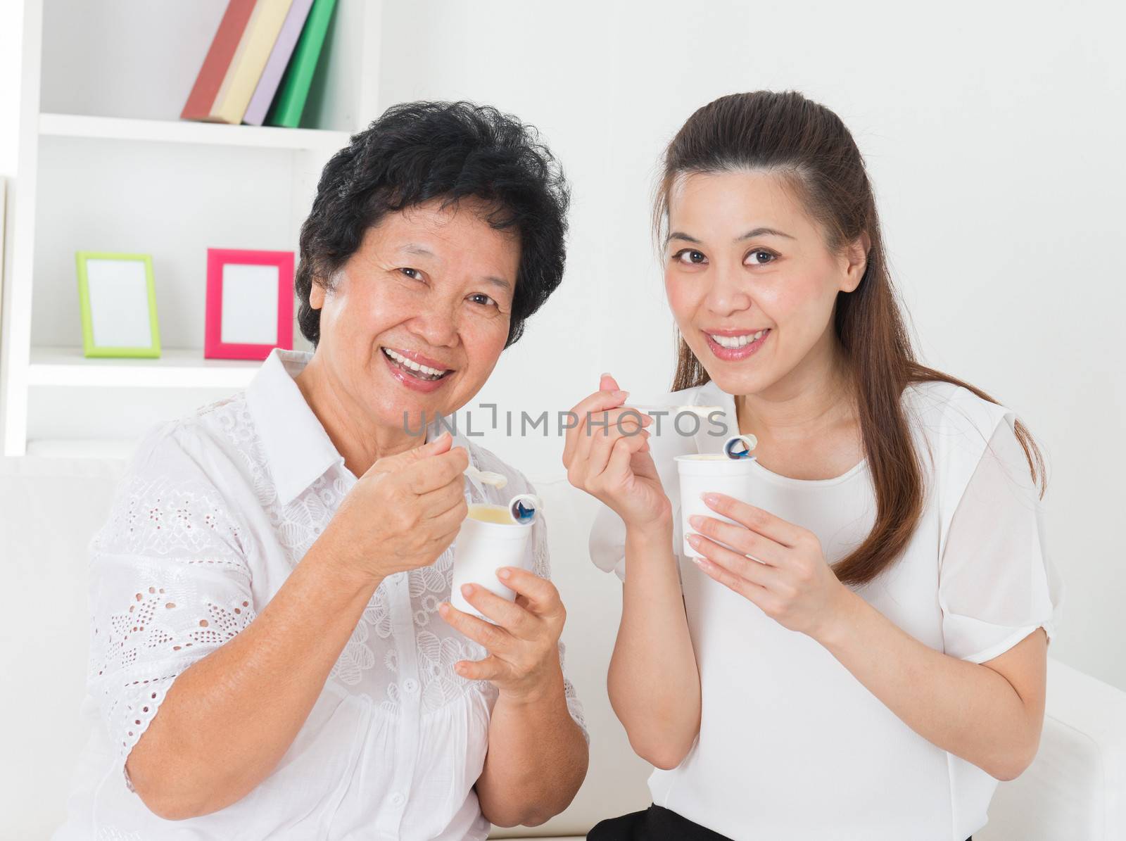 Eating yogurt. Happy Asian family eating yoghurt at home. Beautiful senior mother and adult daughter, healthcare concept.