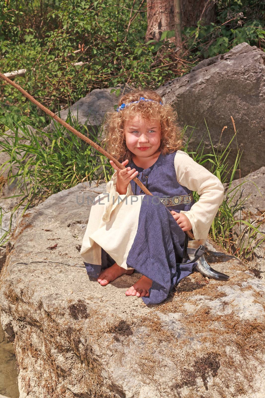 Little girl in medieval dress sitting on a rock while fishing