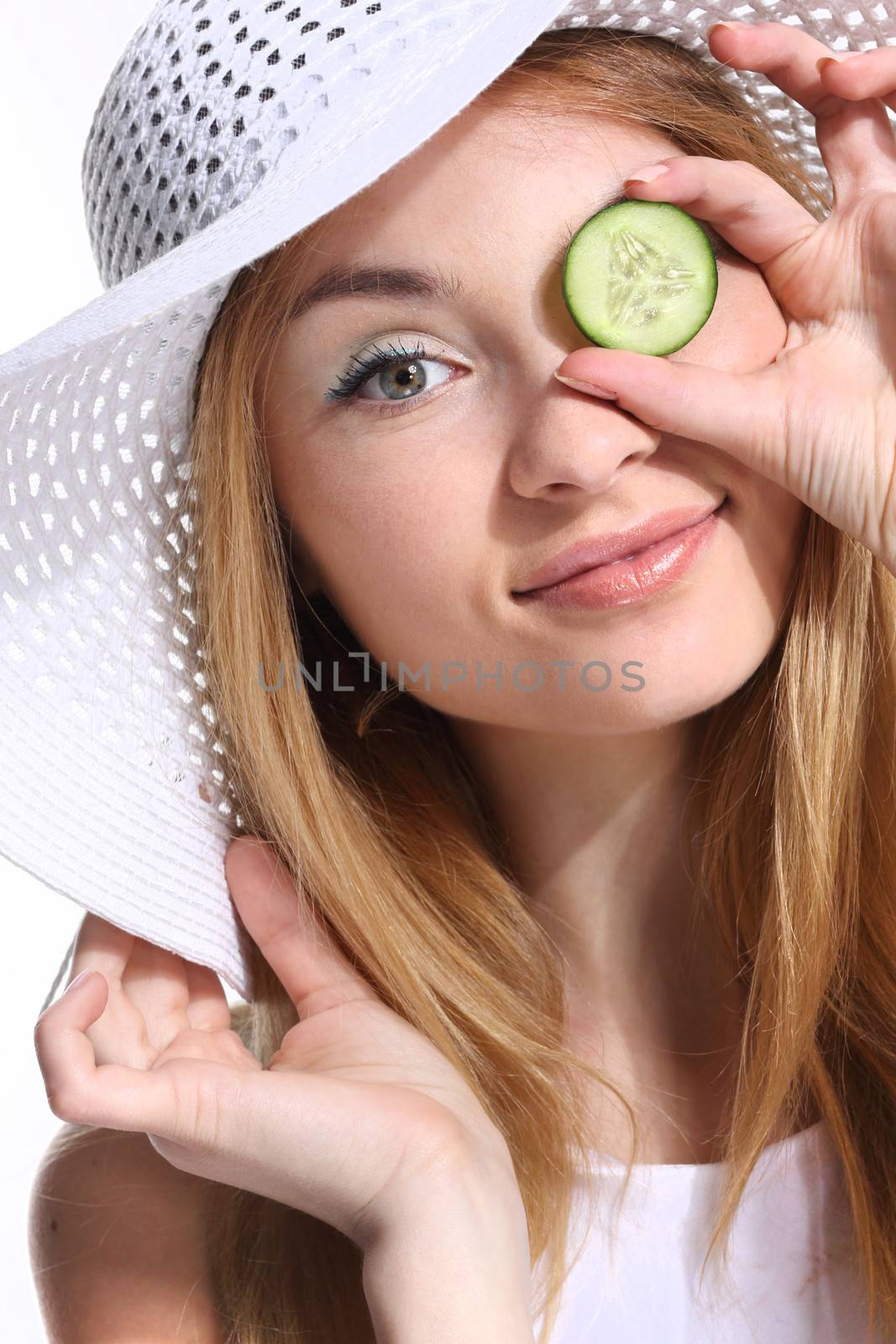 Portrait of young adult Caucasian woman on white background holding cucumber slices over her eyes.