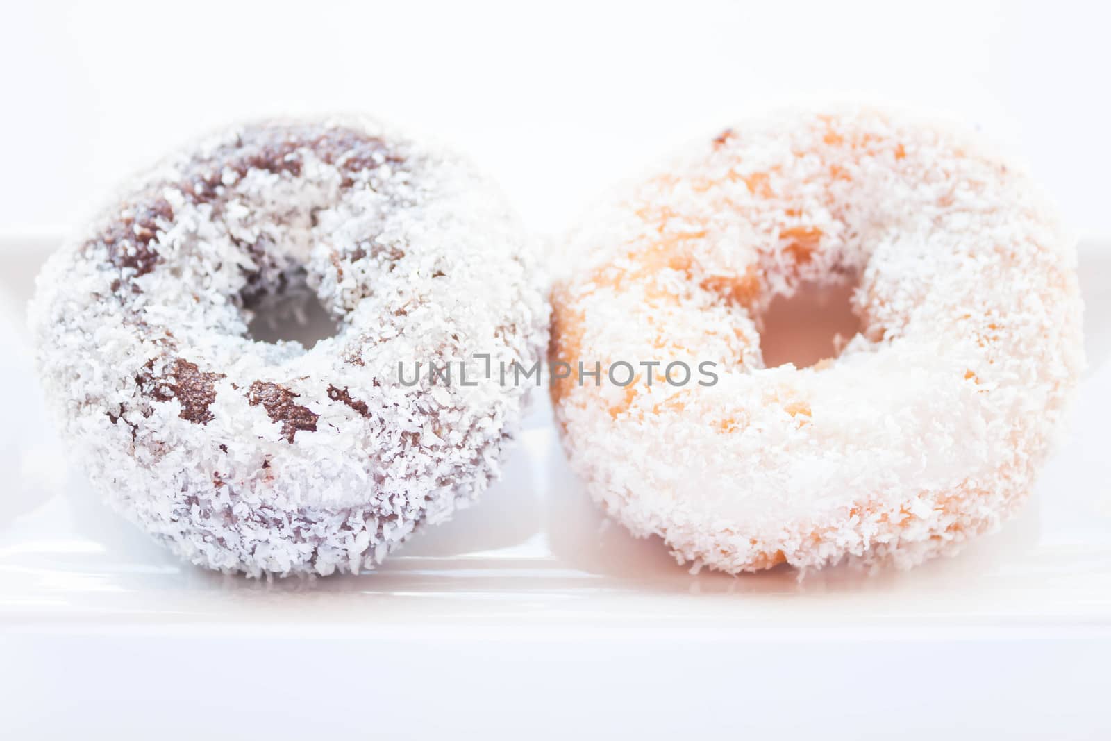 Chocolate and vanilla coconut donuts on white plate, stock photo