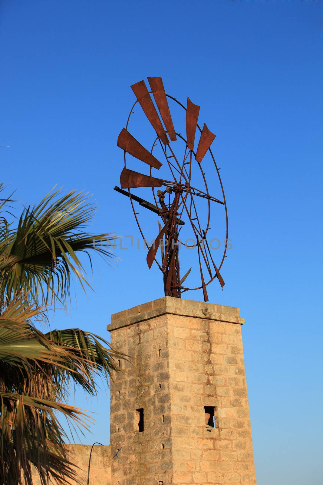 Old broken down windmill with missing vanes mounted on top of an old stone building