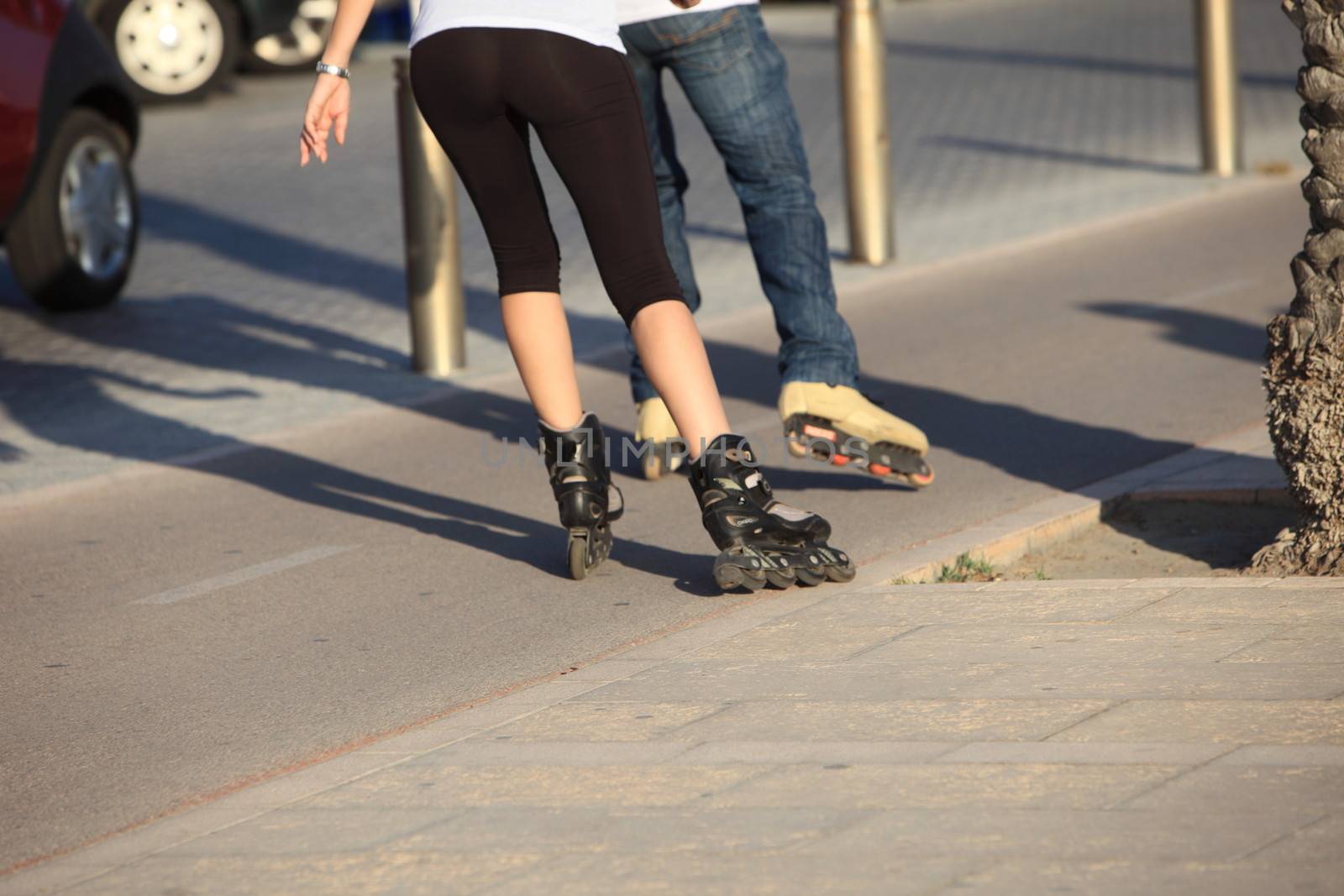 Cropped view of the legs of people rollerblading down an urban sidewalk going away from the camera