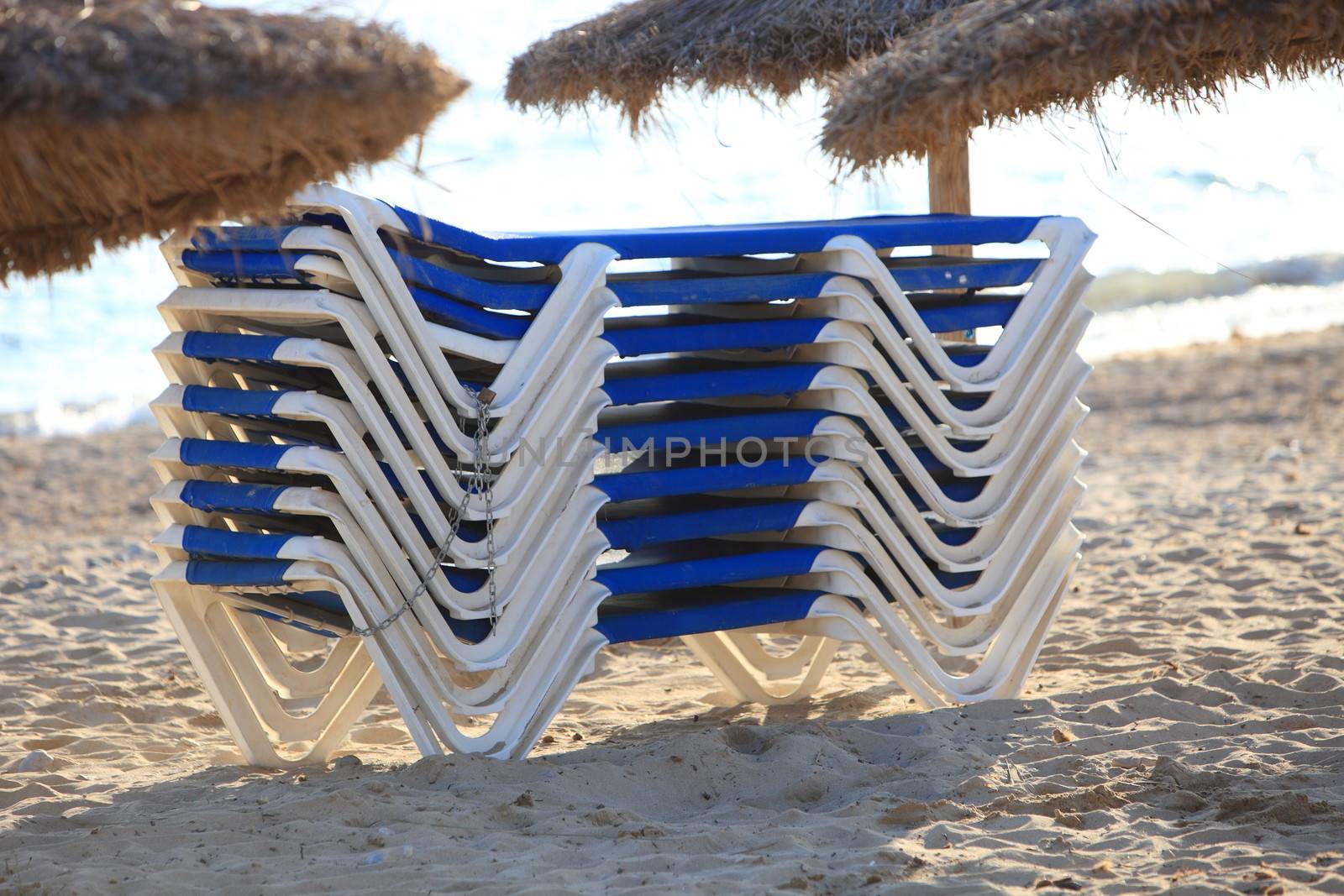Stack of recliner chairs on a sandy tropical beach with traditional thatched umbrellas at a summer holiday resort