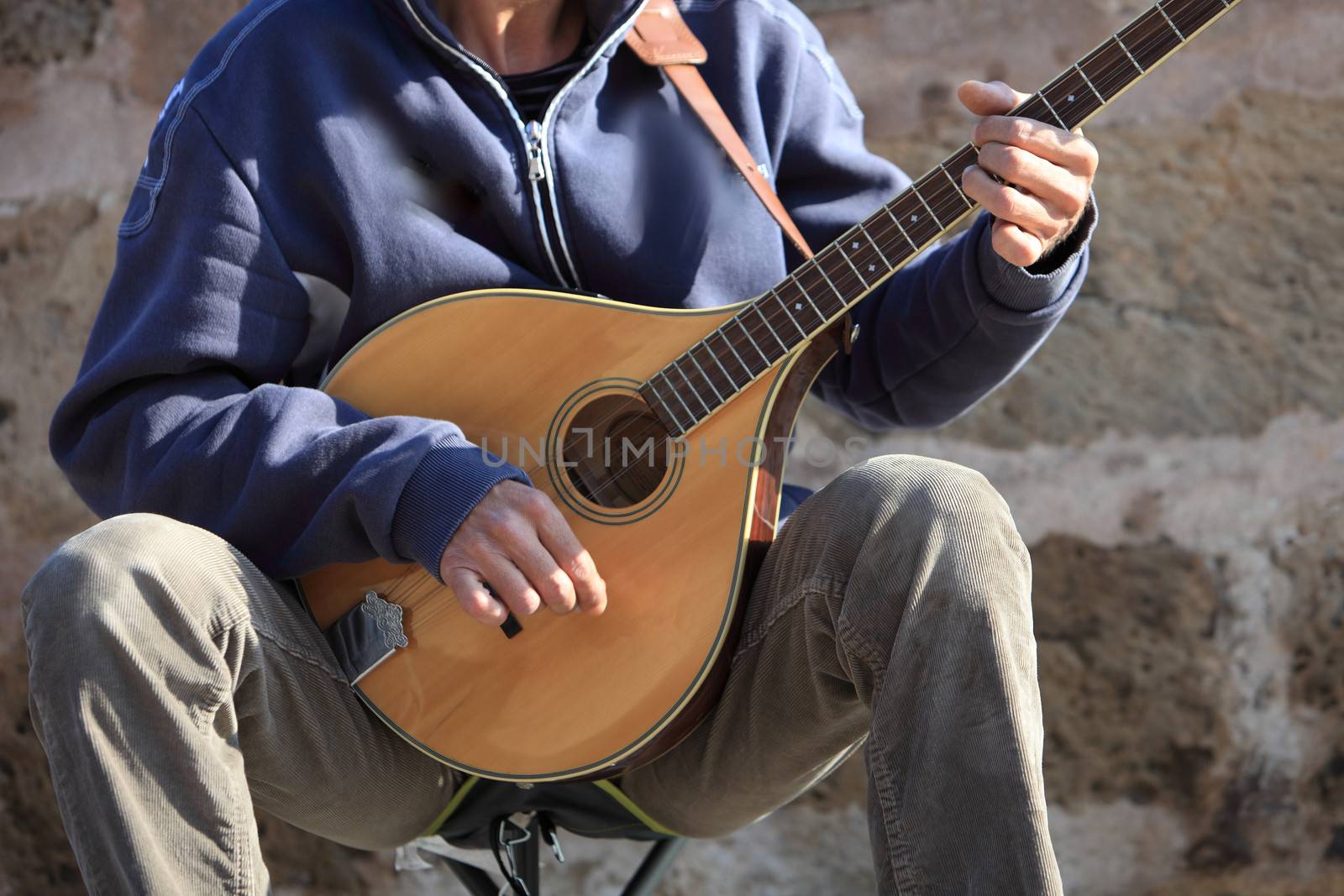 Closep of a man playing a mandolin plucking the strings while sitting in the street