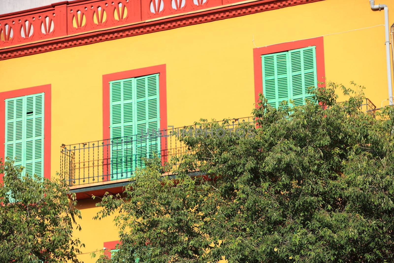 Colourful yellow house with closed green shutters and an orange frame surrounding the windows, exterior facade in sunshine