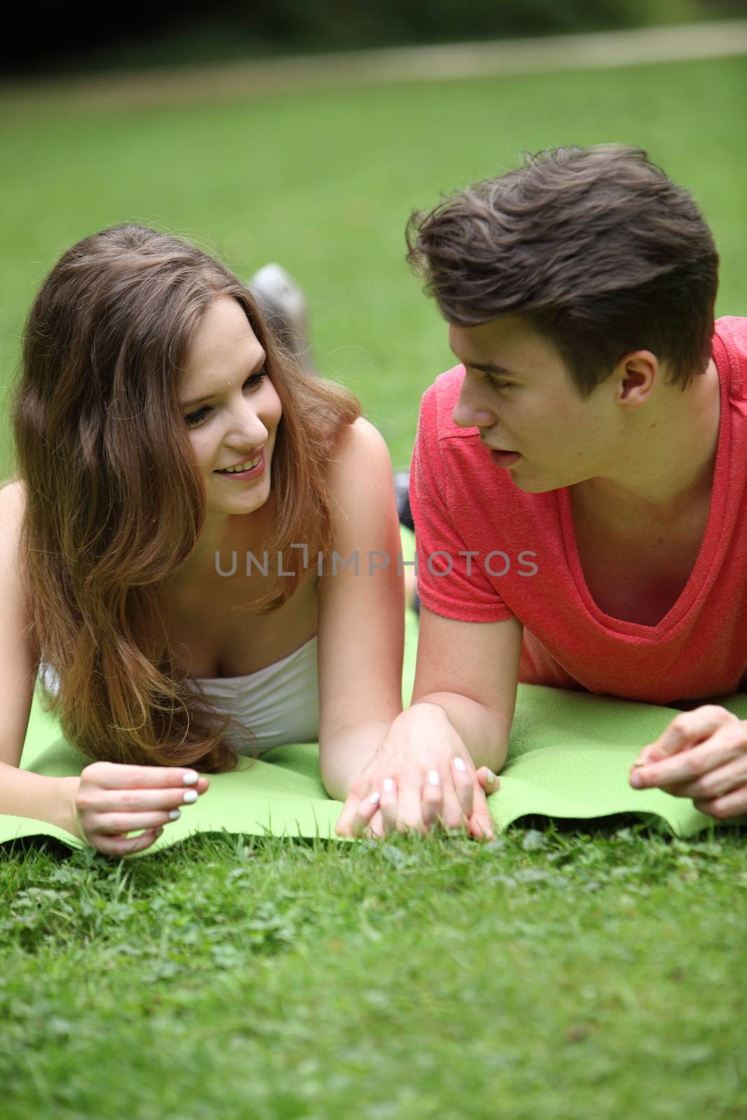 Assectionate teenage couple on a date lying holding hands on a rug in the park chatting and looking into each others eyes
