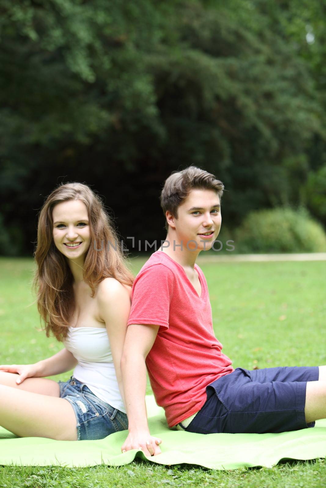Young teenage couple enjoying the summer sunshine sitting back to back on the grass in a lush green garden