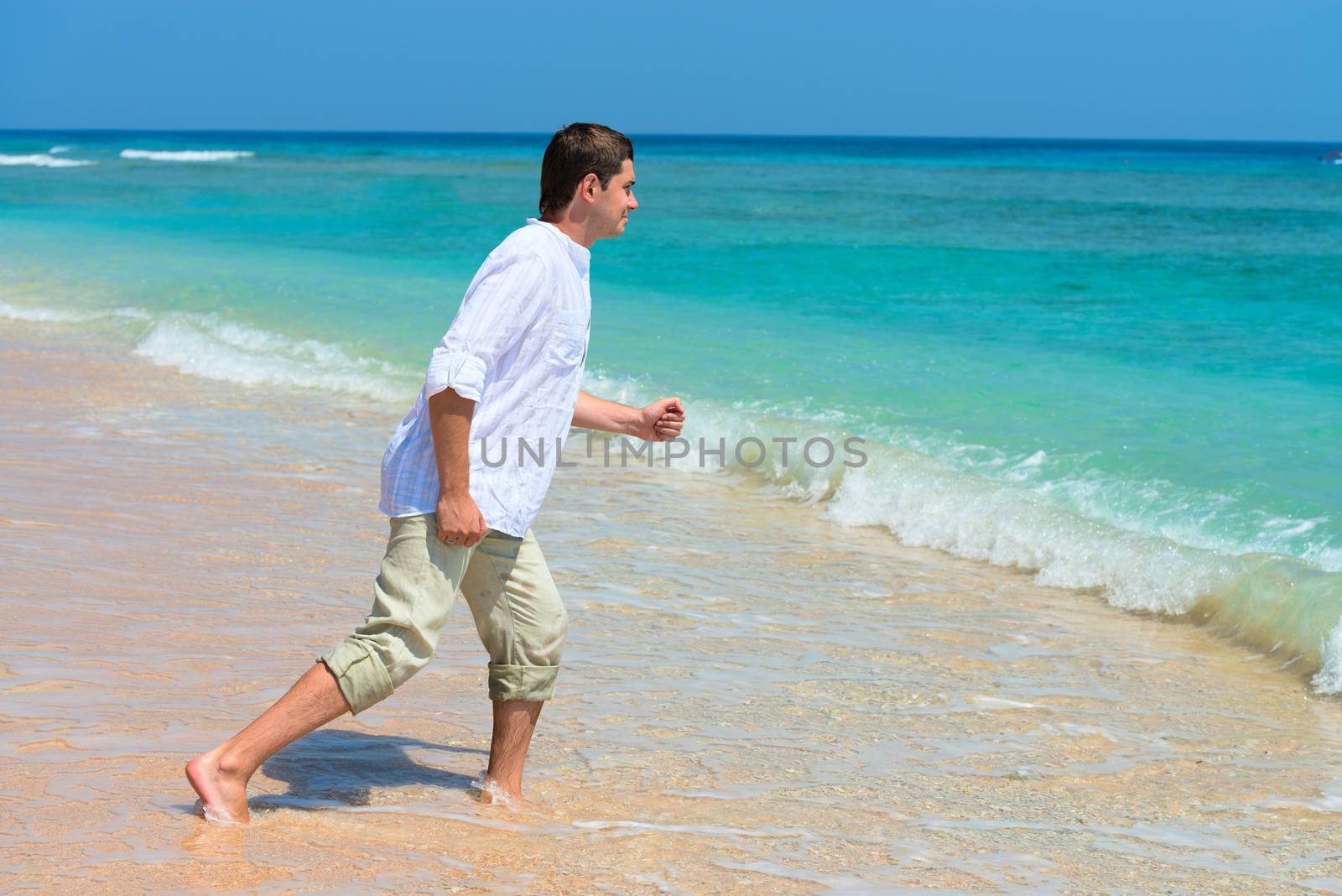 Man run in the blue sea in his dress with desire to dive in clean tropical water
